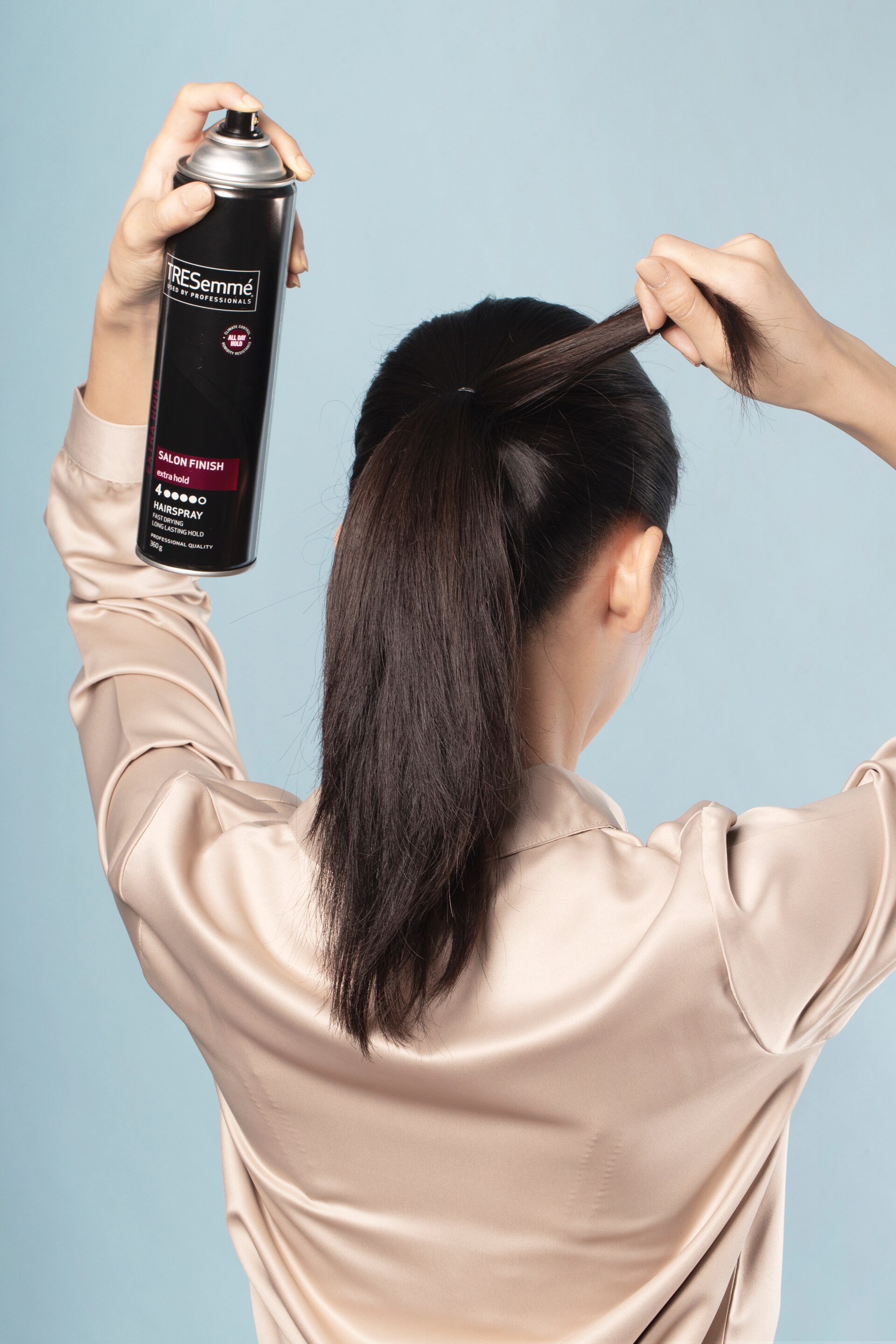 Wanita asia menyemprot bagian rambut ponytail dengan hairspray