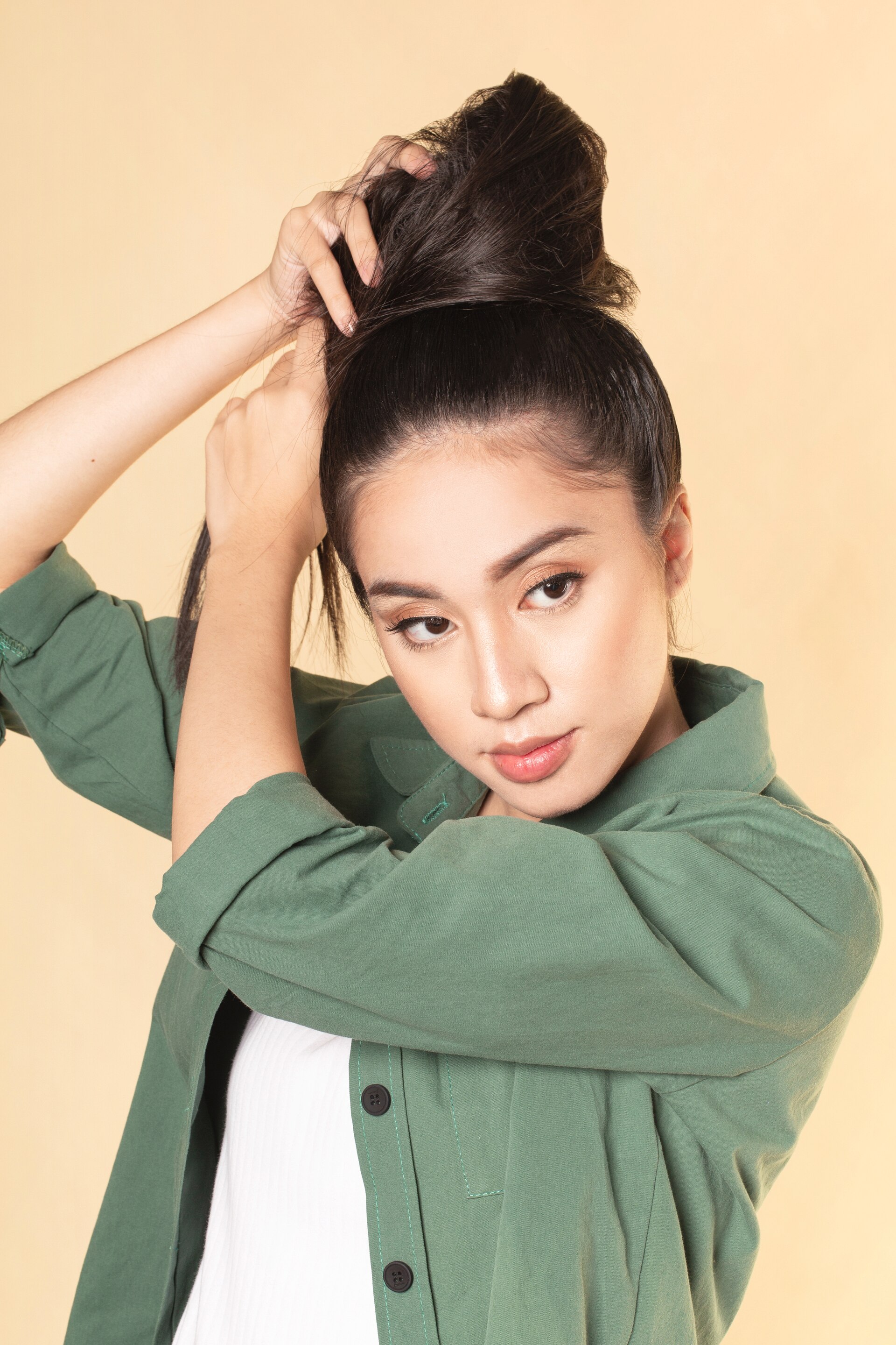 Wanita asia dengan rambut hitam membuat top knot untuk rambut panjang