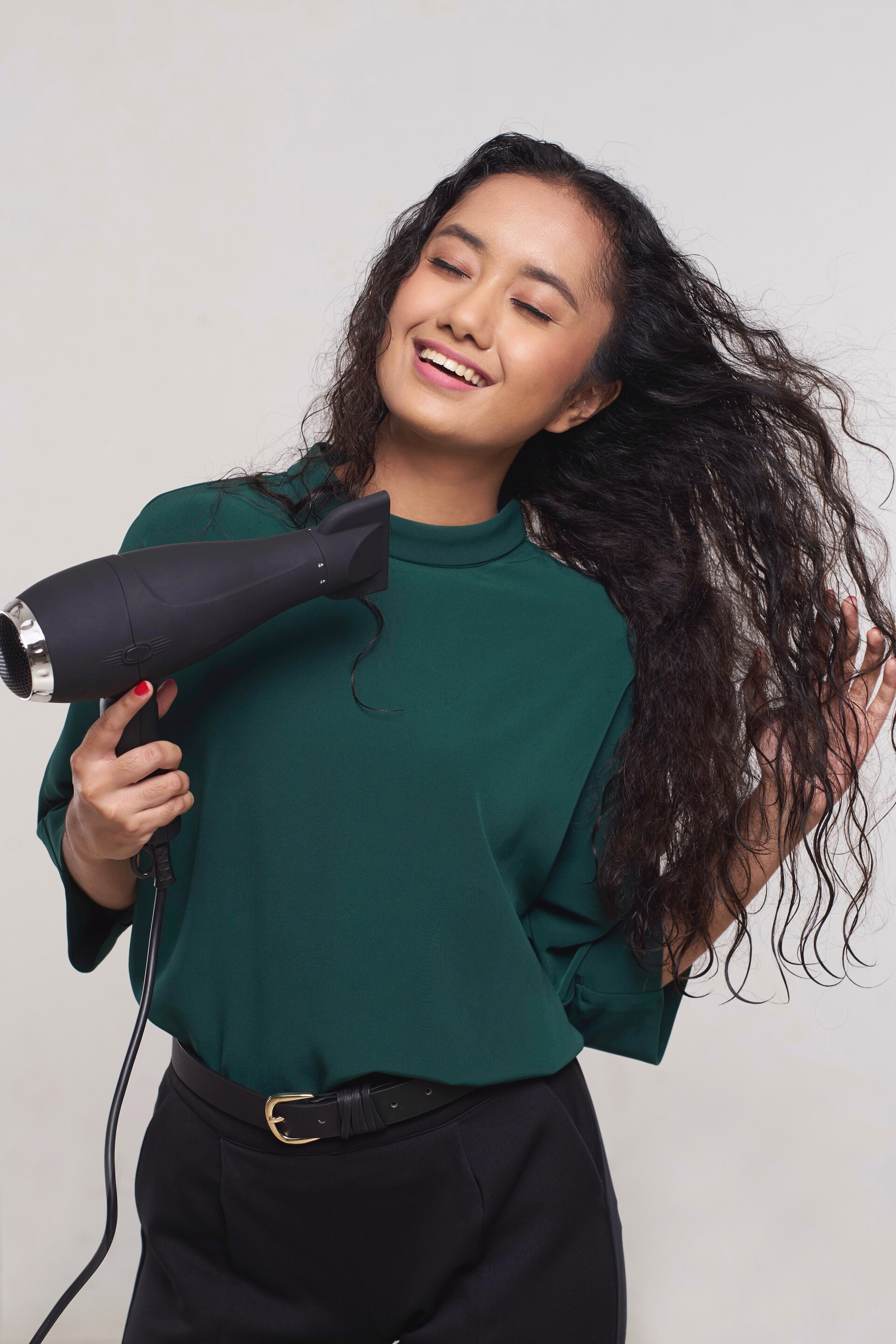 Wanita asia dengan rambut keriting panjang warna hitam menggunakan hairdryer – cara meluruskan rambut keriting.