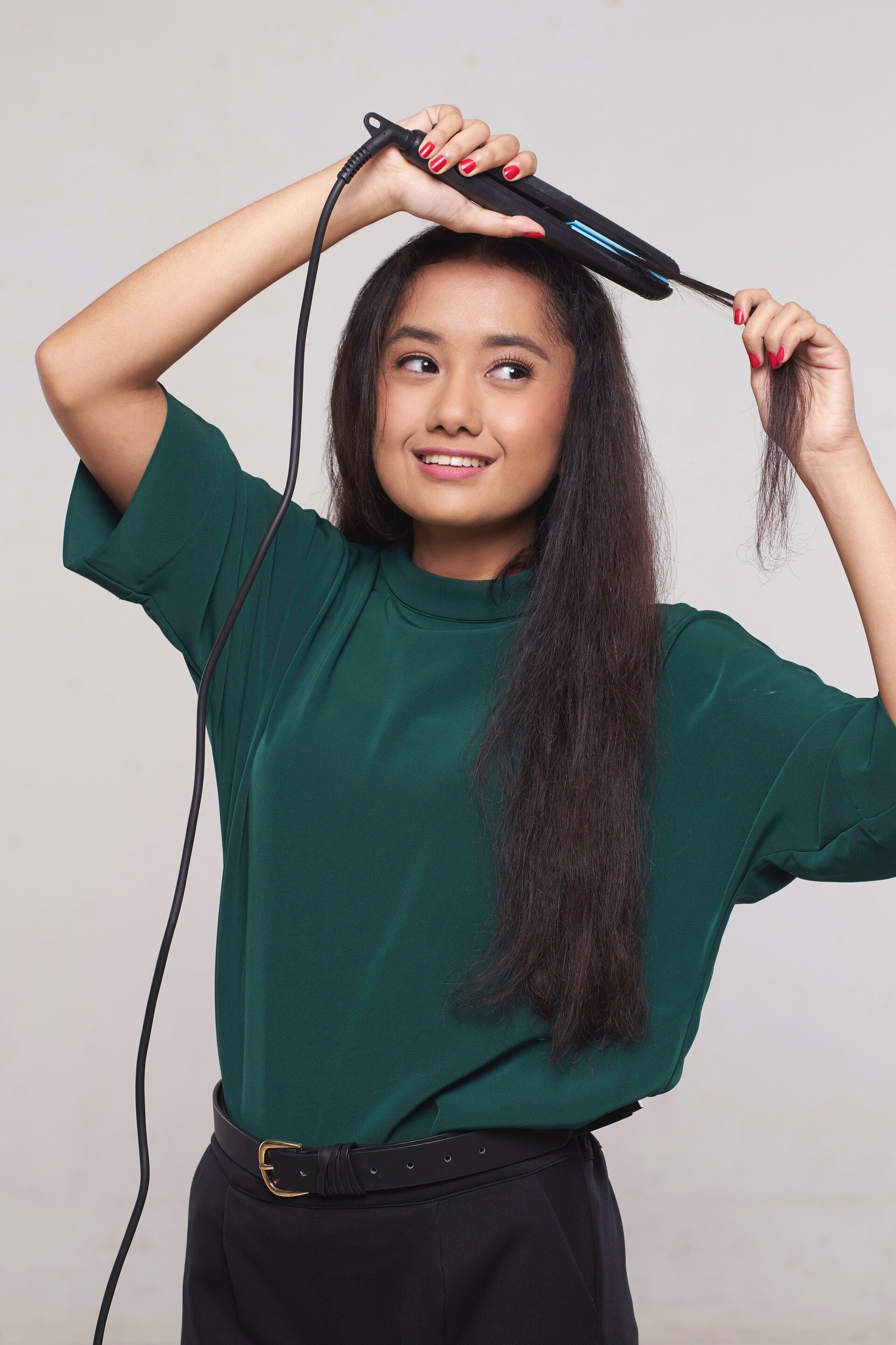 Wanita asia dengan rambut keriting panjang warna hitam mencatok sisa rambut dengan flat iron.