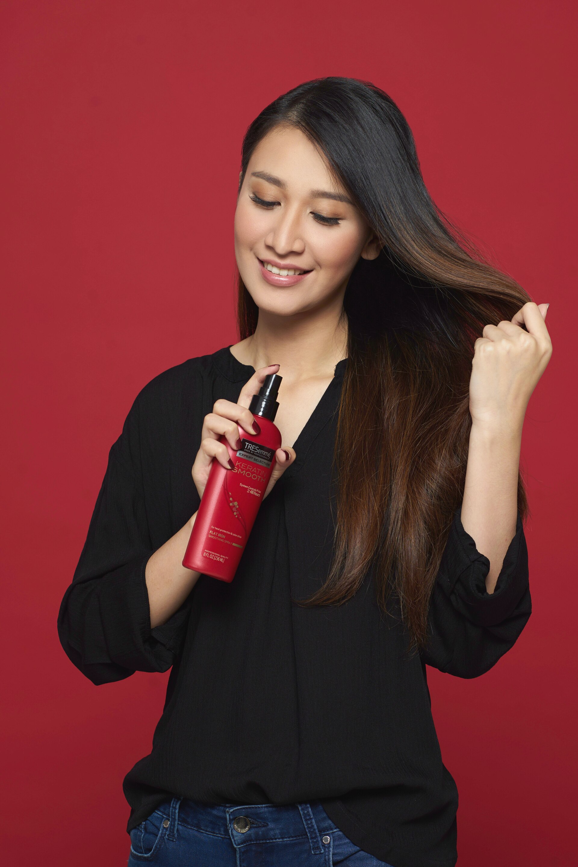 Wanita asia menyemprotkan heat protection spray ke batang rambutnya