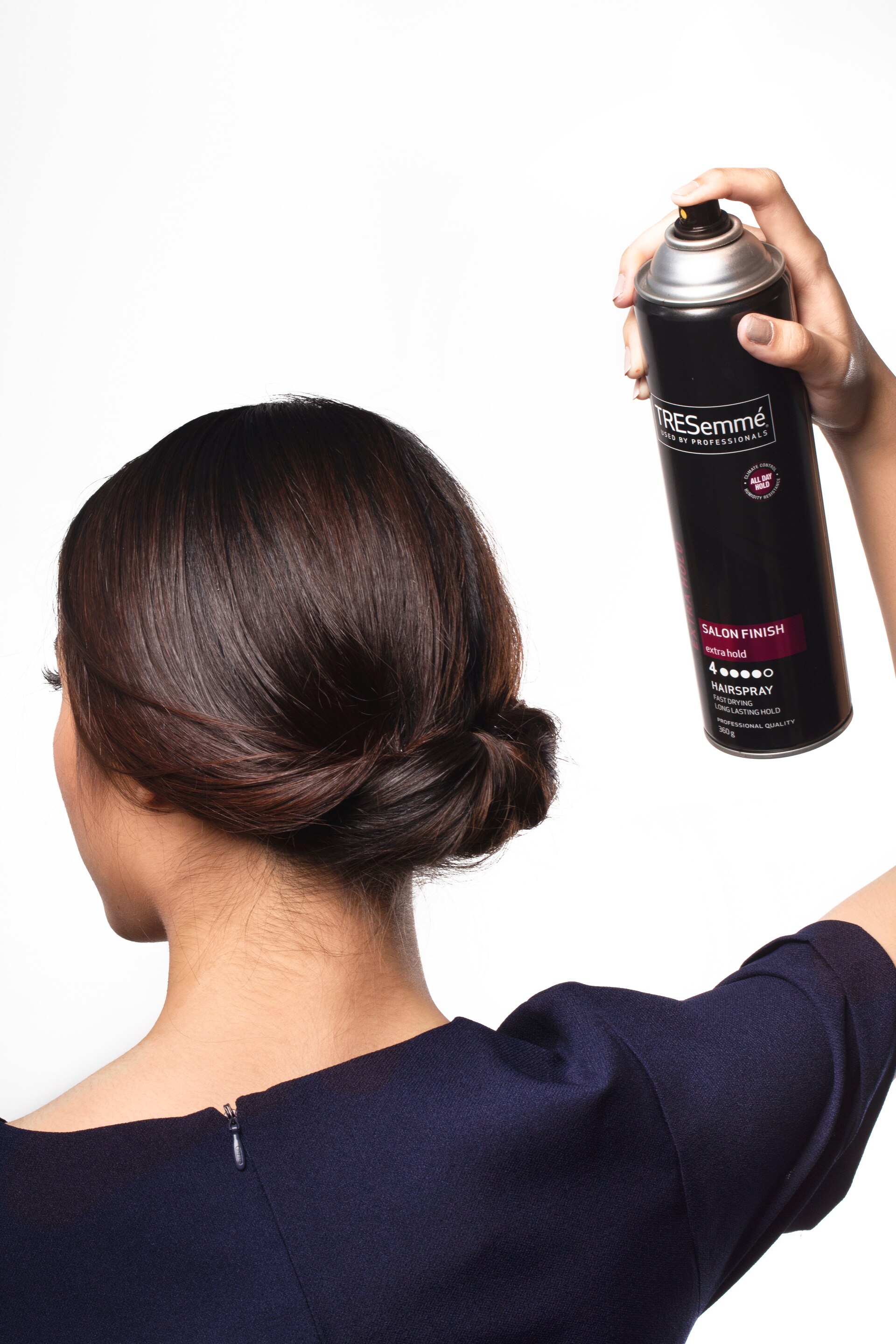 wanita asia berambut hitam sedang menyemprot hairspray untuk sanggul chignon