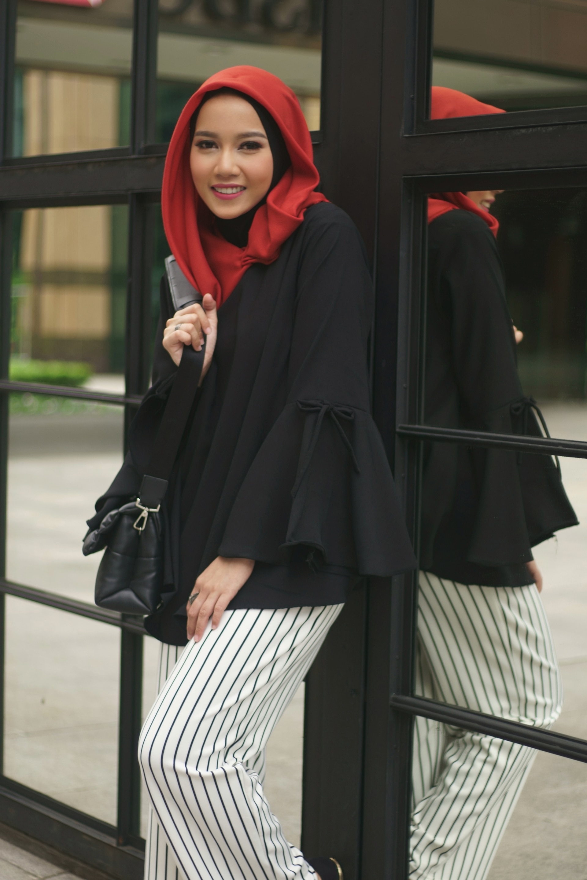 Wanita asia dengan warna hijab merah dan baju hitam menggunakan celana garis-garis hitam