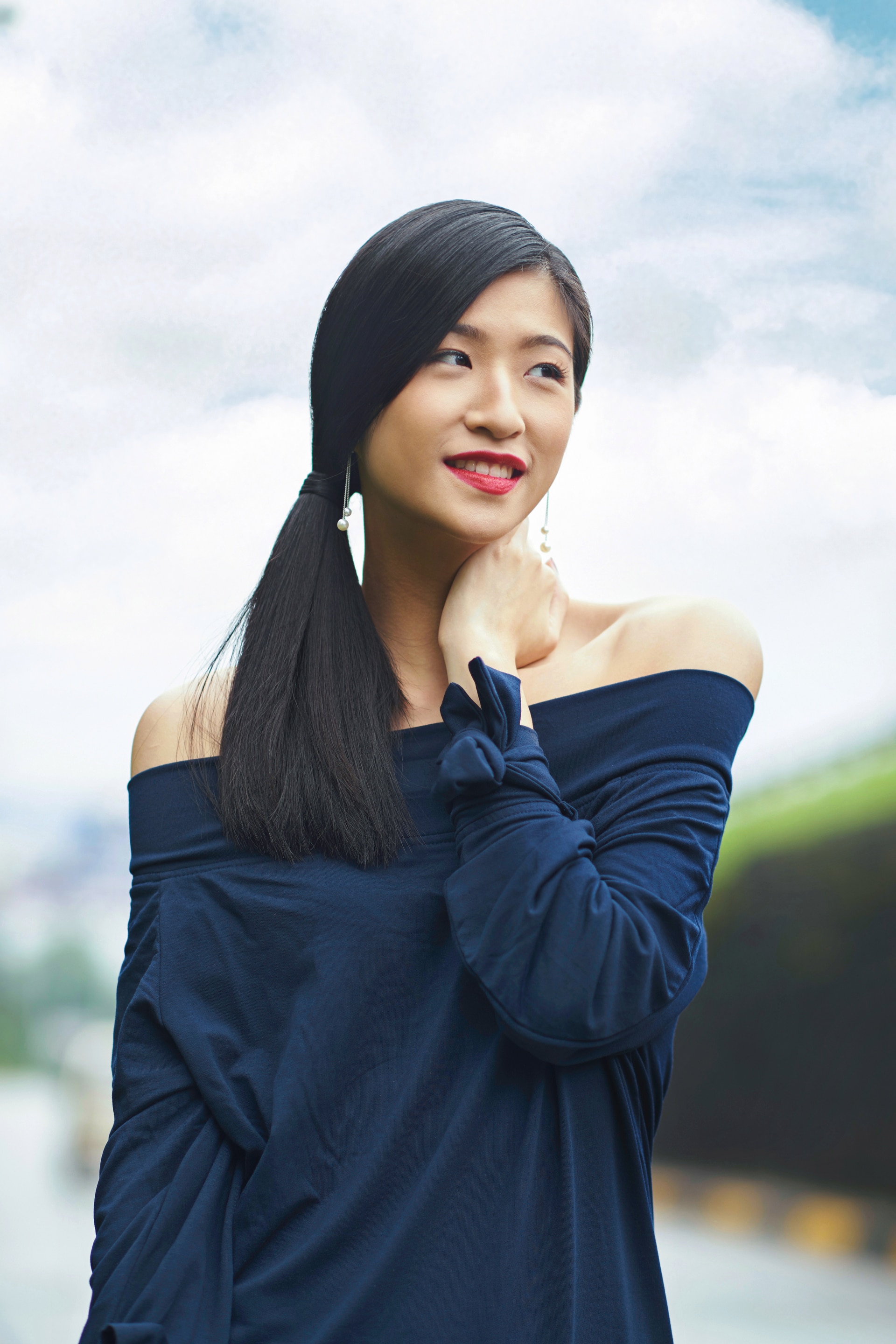 Smiling Asian woman looking away and putting her hand on her neck.