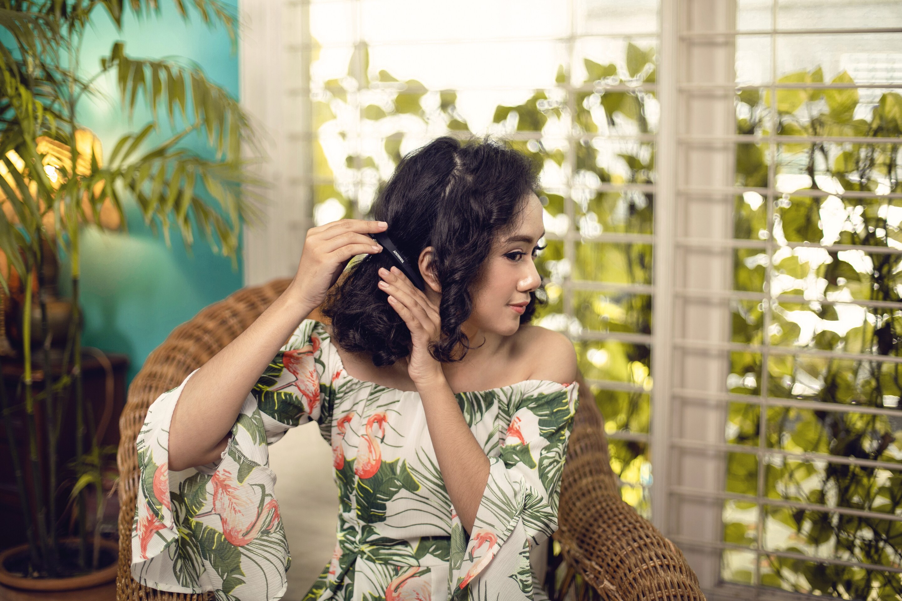 Wanita berambut keriting sedang menjepit rambut bagian belakang.