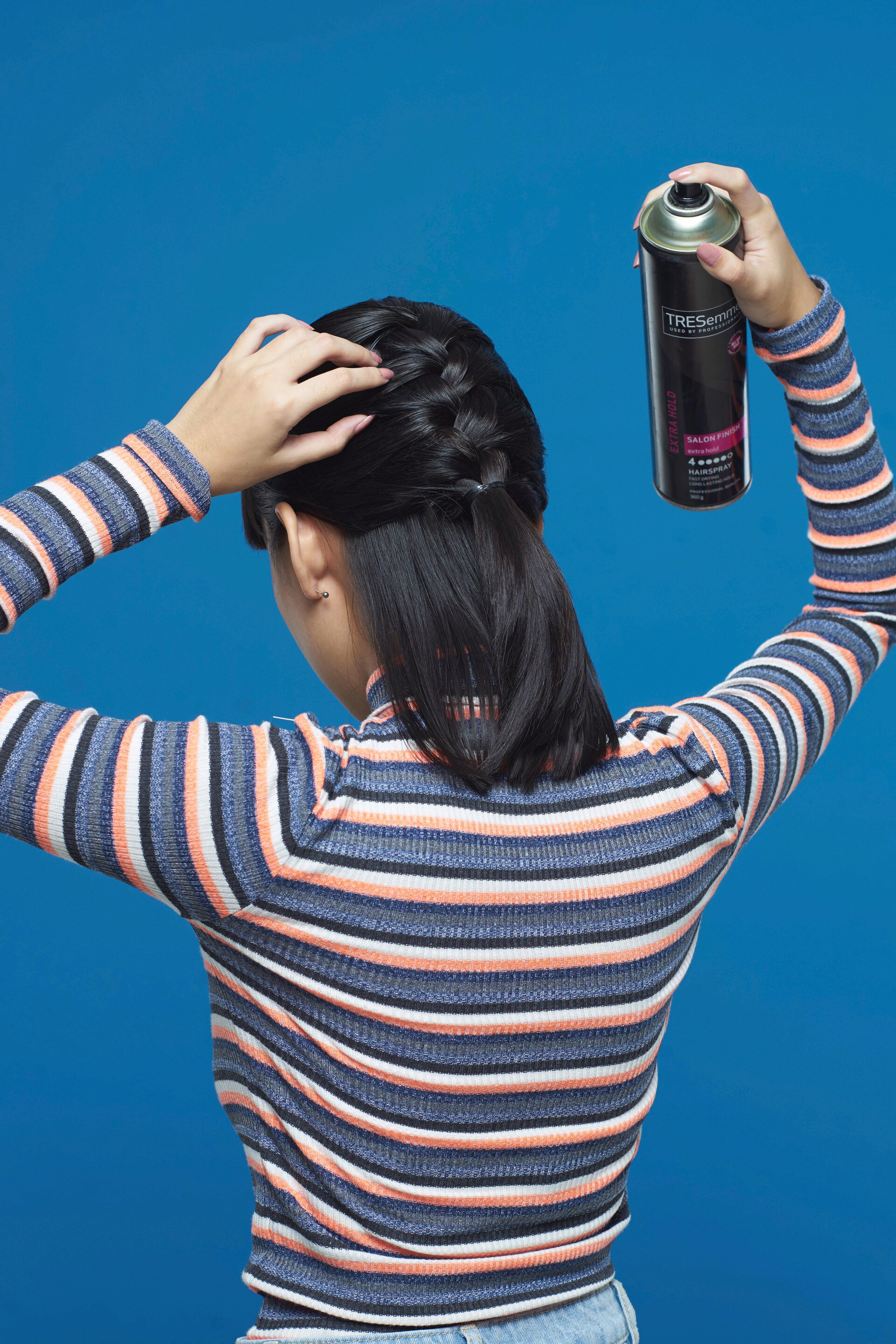 Wanita asia dengan rambut pendek hitam menyemprotkan hairspray pada kepang rambut