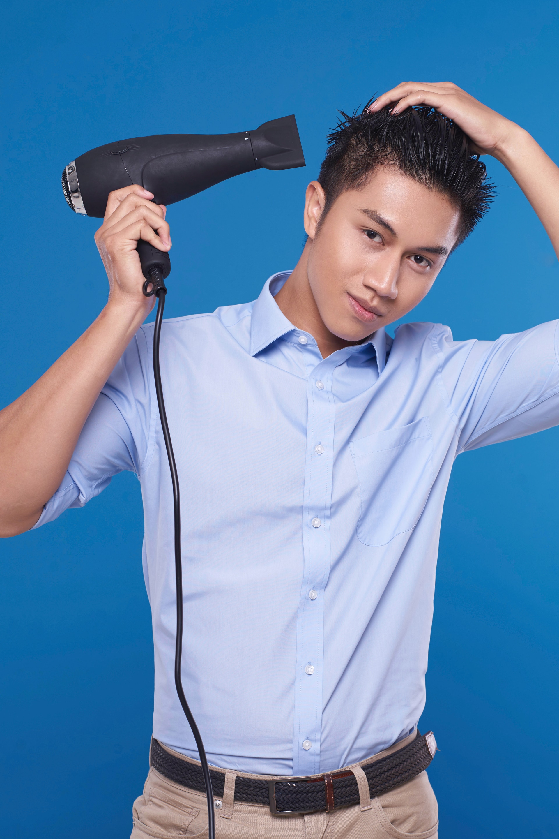 Pria asia dengan warna rambut hitam sedang mengeringkan rambut dengan hairdryer – tutorial menata gaya rambut pompadour