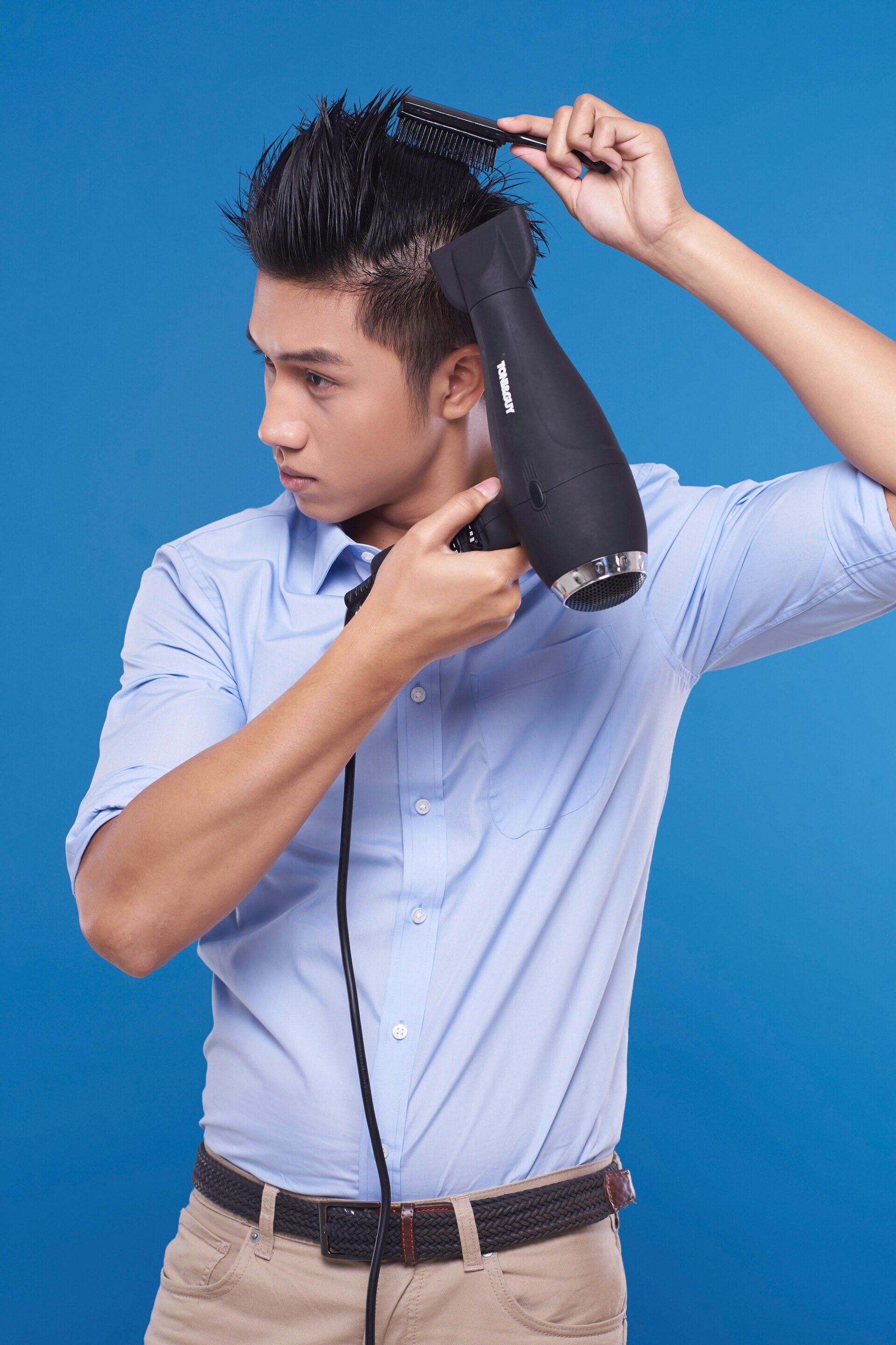 Pria asia dengan warna rambut hitam sedang menyisir rambut sambil mengeringkan – tutorial menata gaya rambut pompadour