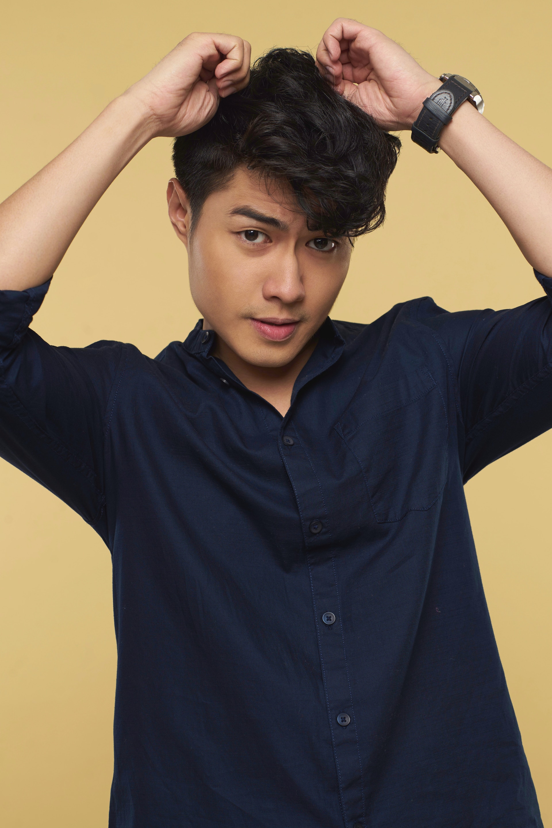 Pria asia dengan rambut hitam keriting pendek sedang memegang rambut.