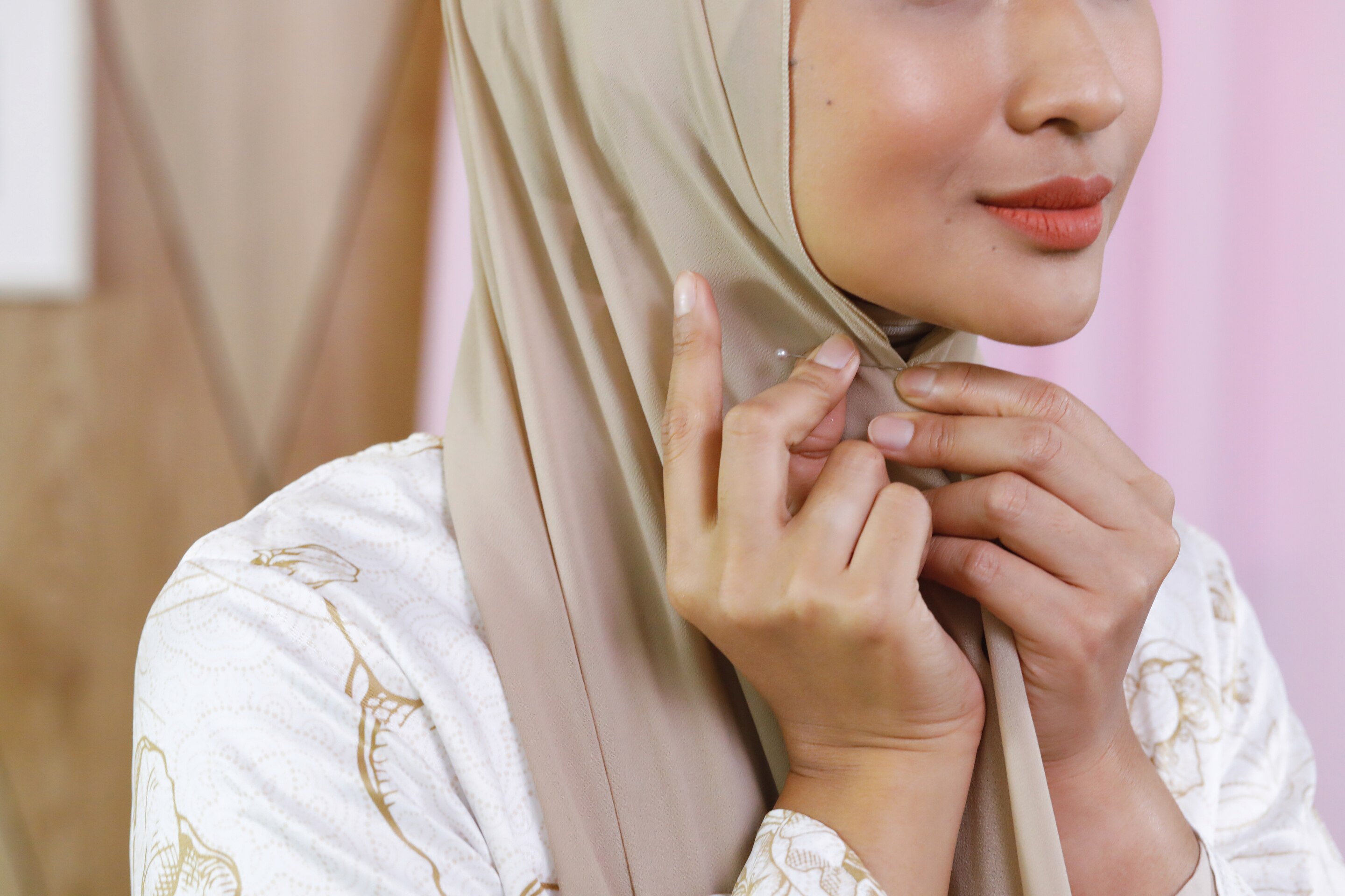 Wanita Asia sedang merekatkan hijab dengan jarum pentul di bawah dagu