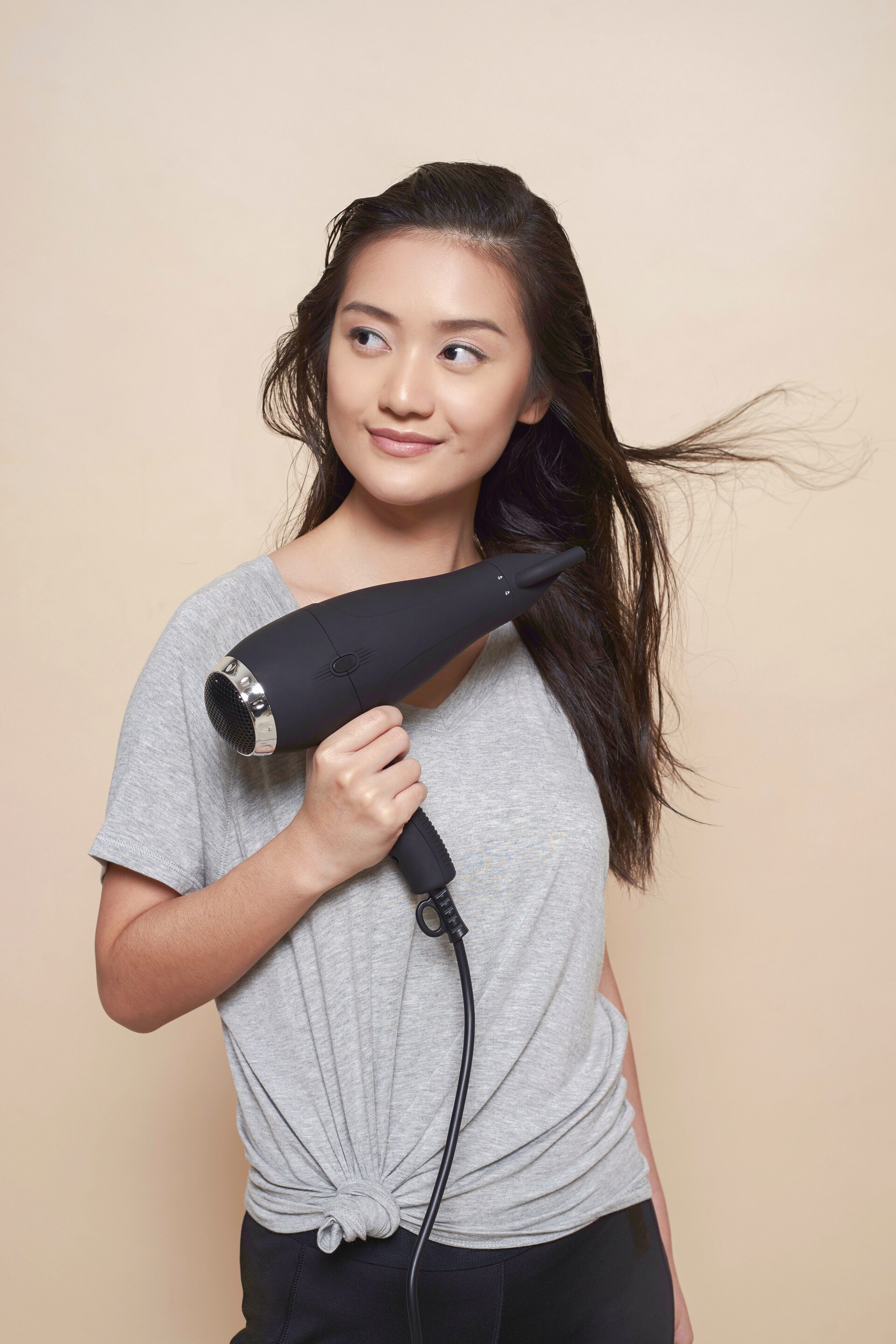 Wanita dengan warna rambut hitam menggunakan atasan abu-abu sedang mengeringkan rambut