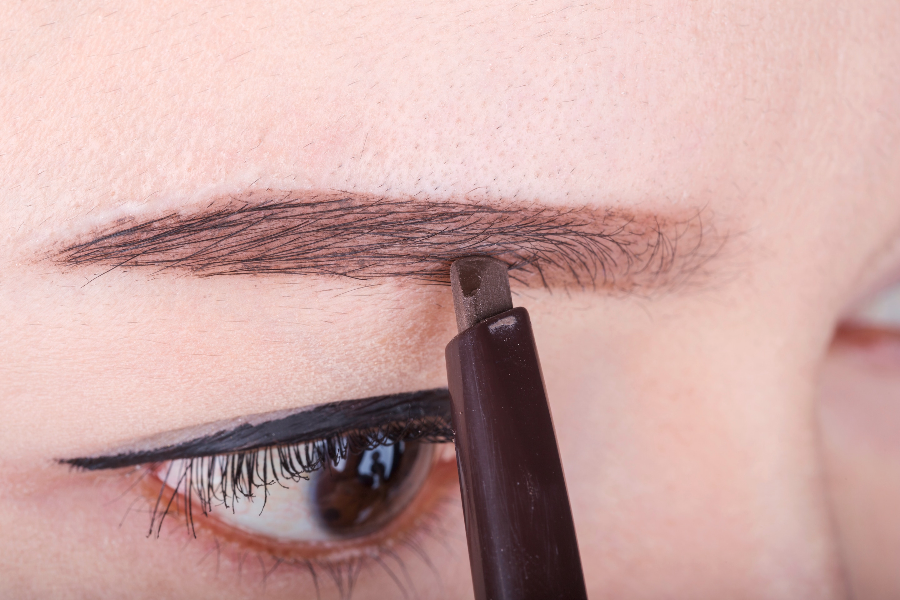 Closeup of an Asian woman drawing her eyebrows with a brow pencil
