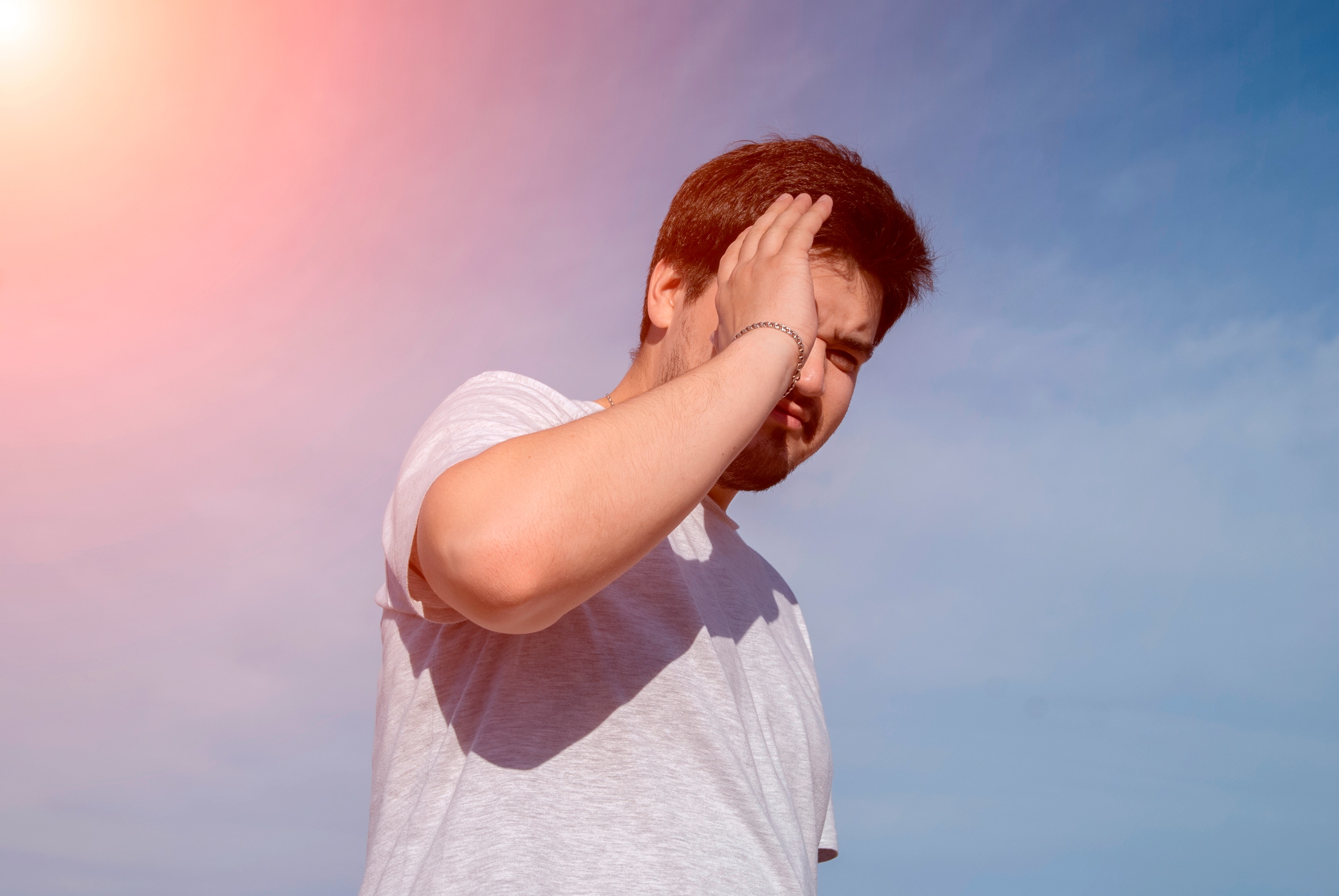 An Asian man standing under the sun and shielding his eyes from sunlight