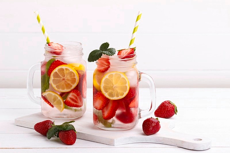 Dua gelas infused water berisi buah stroberi dan buah lemon serta daun mint
