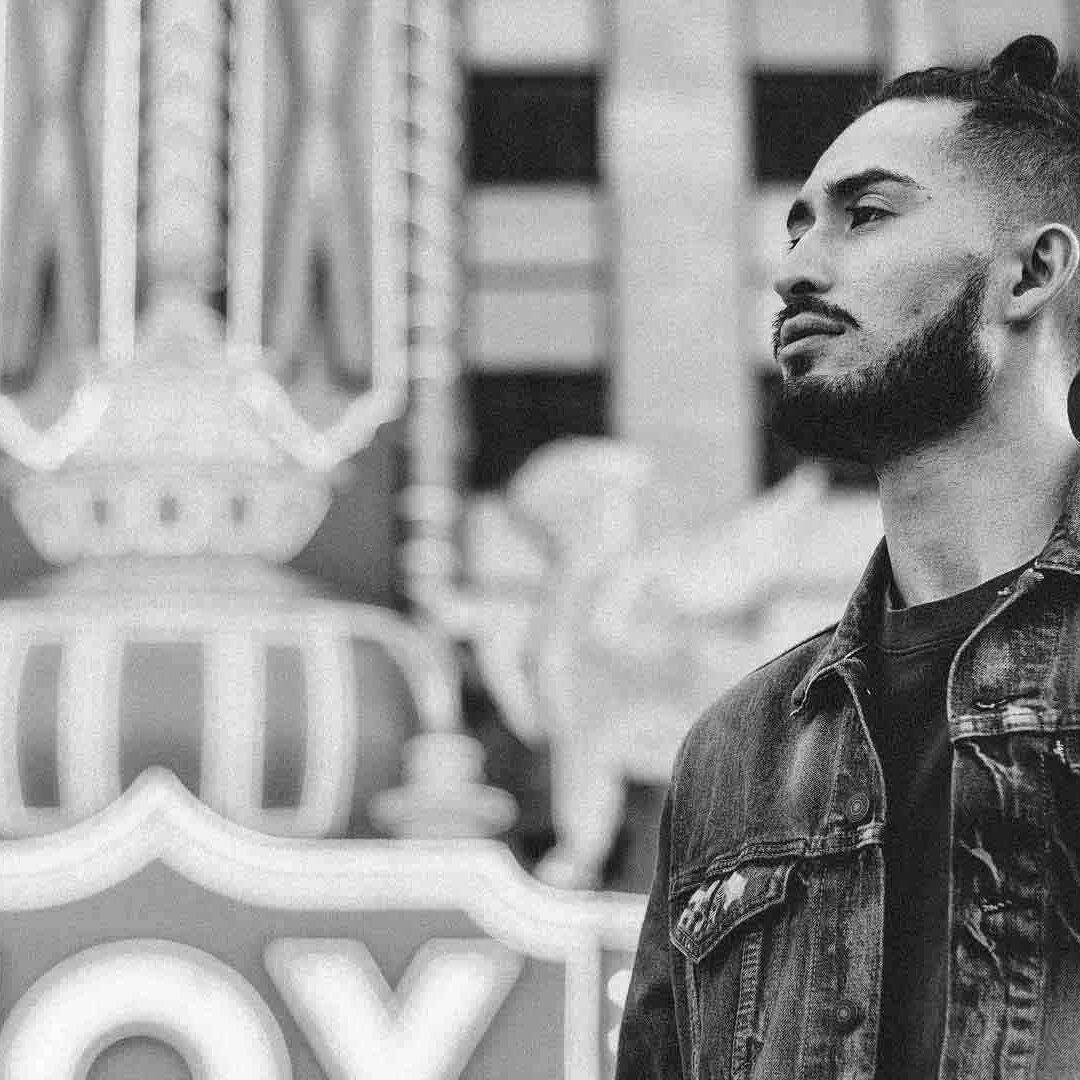 A bearded guy in the city, wearing a denim jacket.