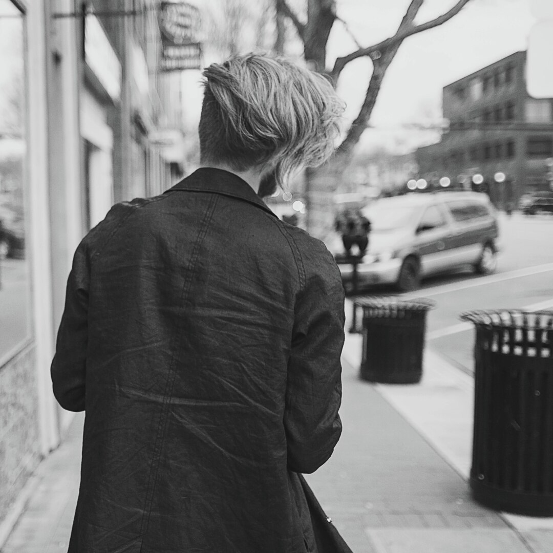 A guy with long hair, walking down a city street. 
