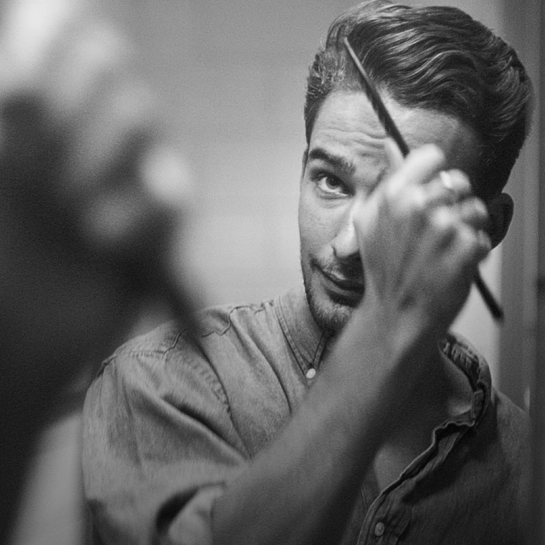 Un hombre peinando su tupé frente al espejo.