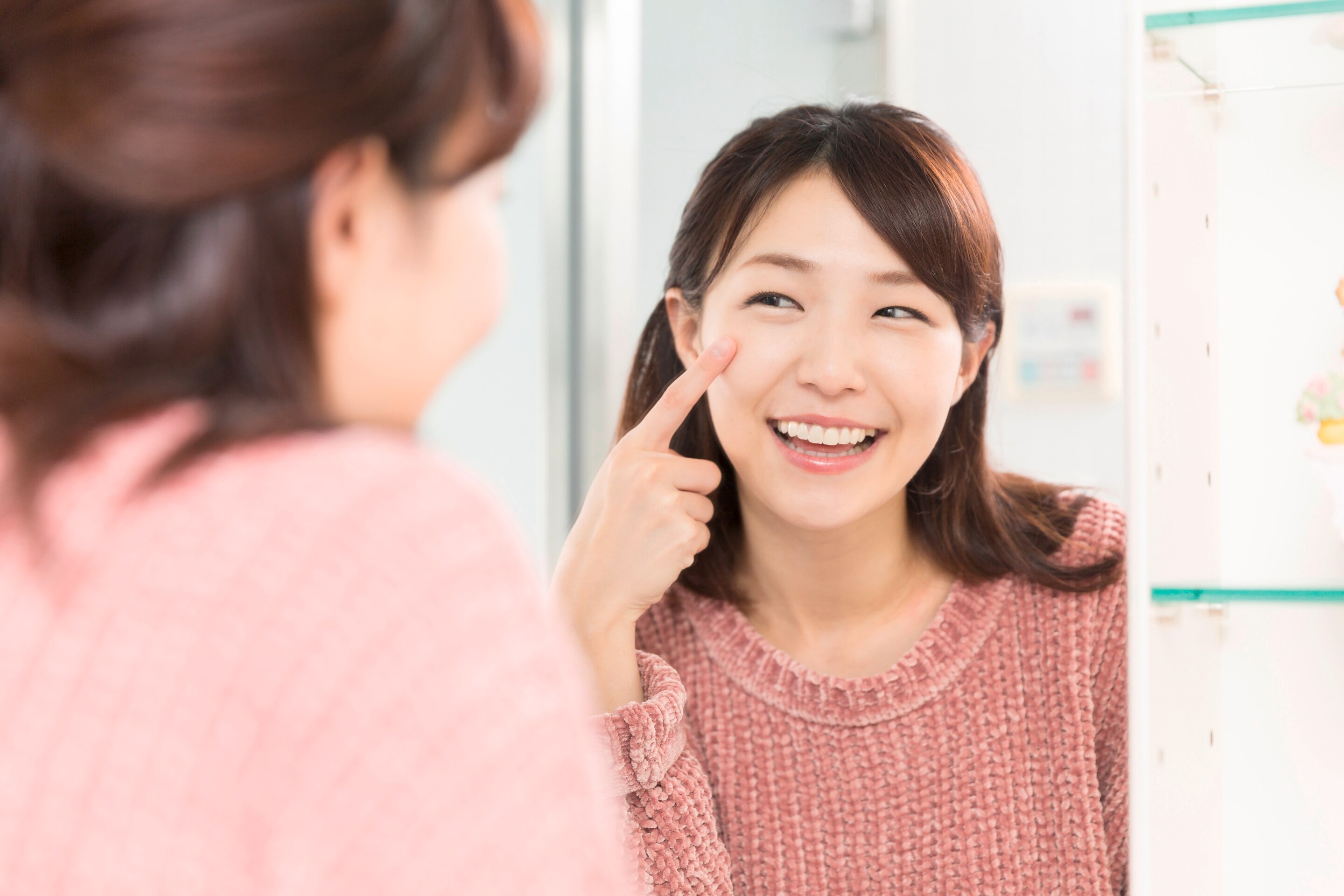 An Asian woman pointing to her skin in the mirror