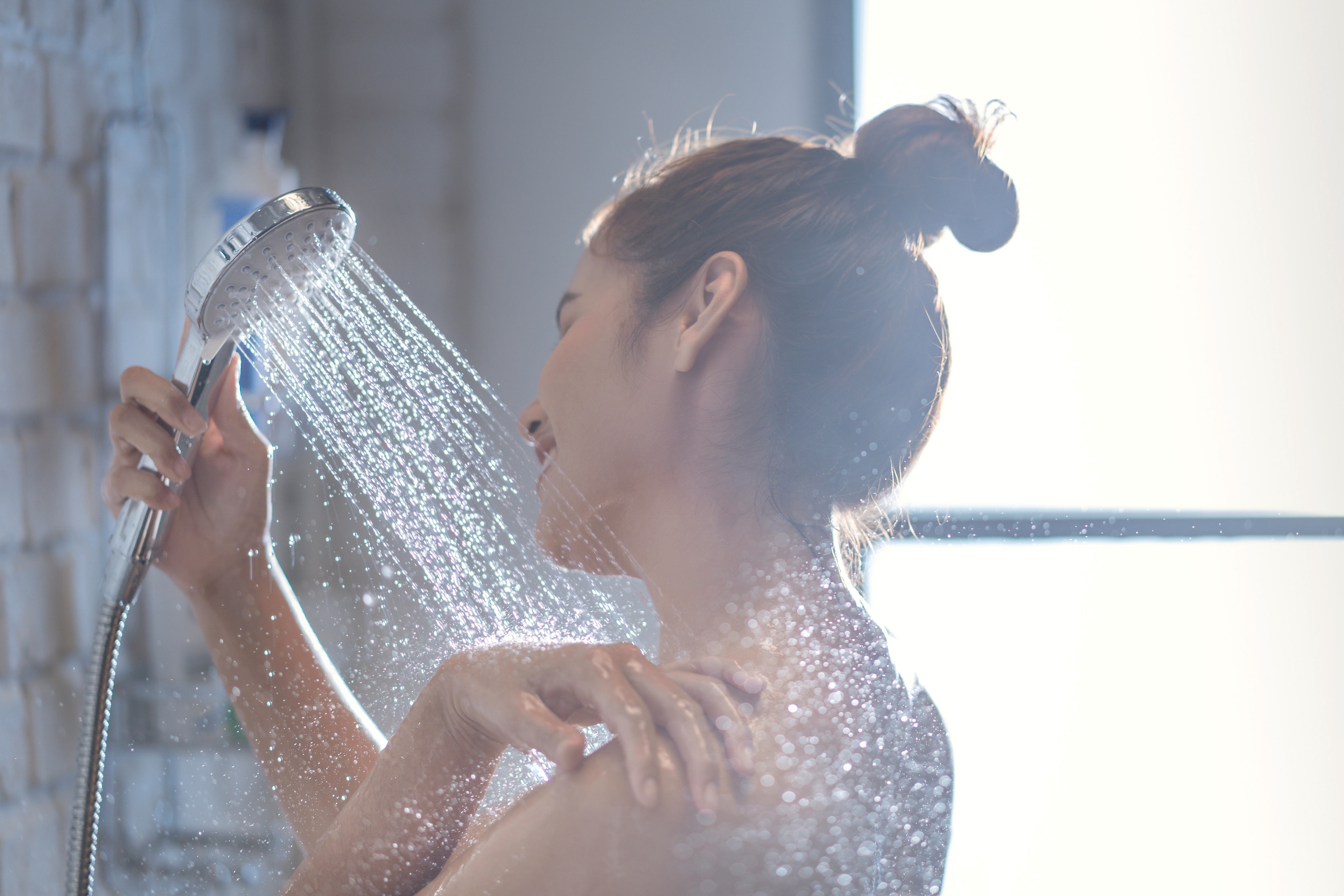 Asian woman with her hair up in a bun taking a shower. 