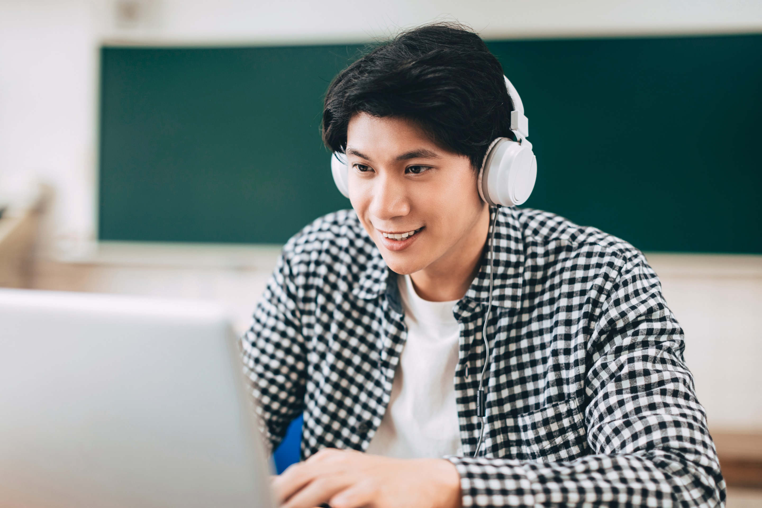 pria asia sedang kuliah online menggunakan laptop dan headphones