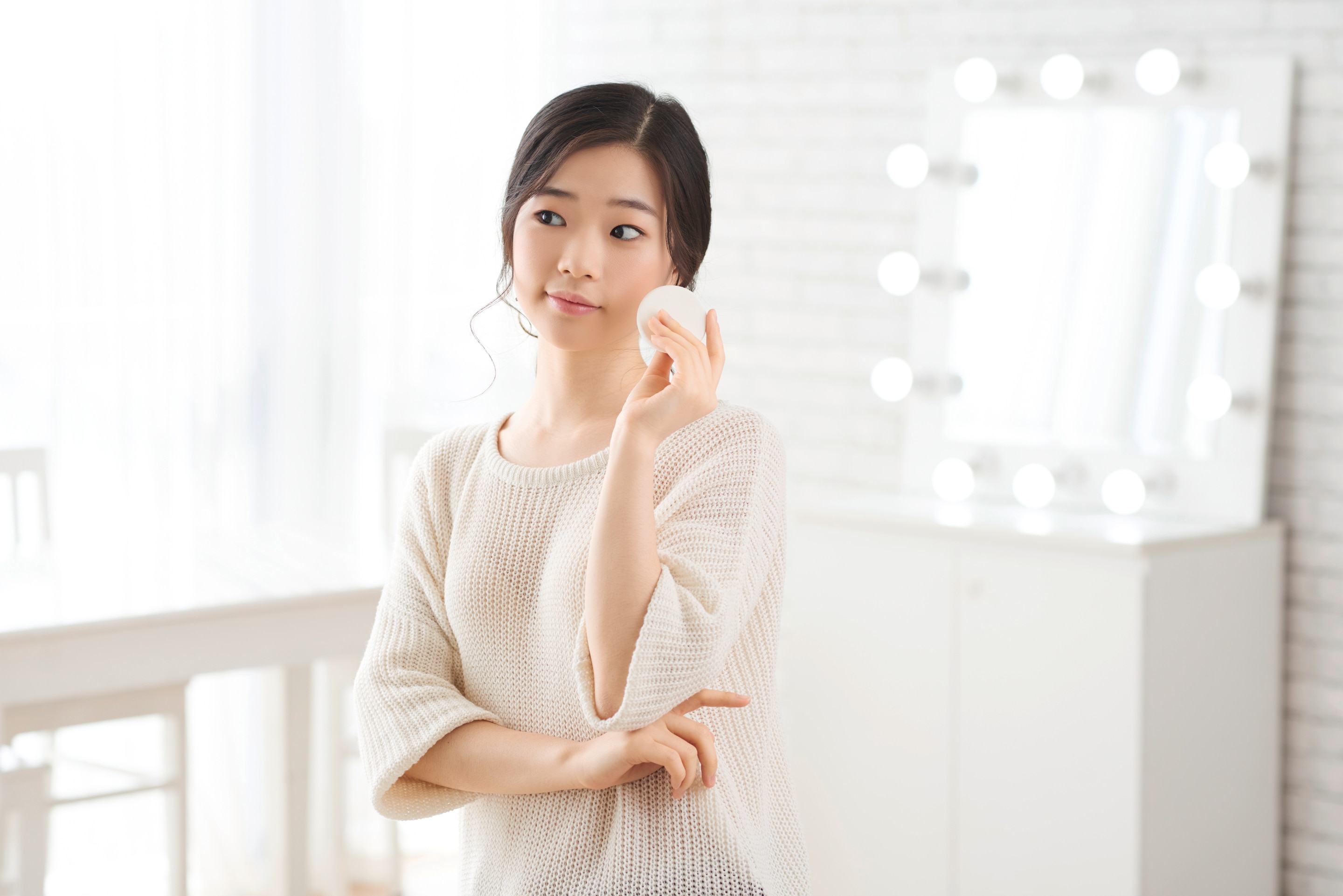 A woman applying toner using a cotton pad on her face.