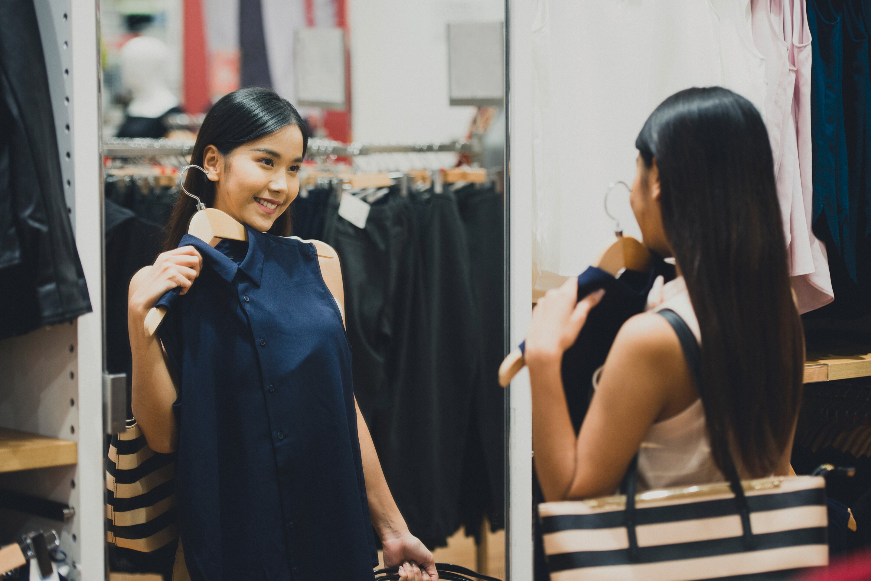 A woman putting a blue top against herself in front of a mirror in a store