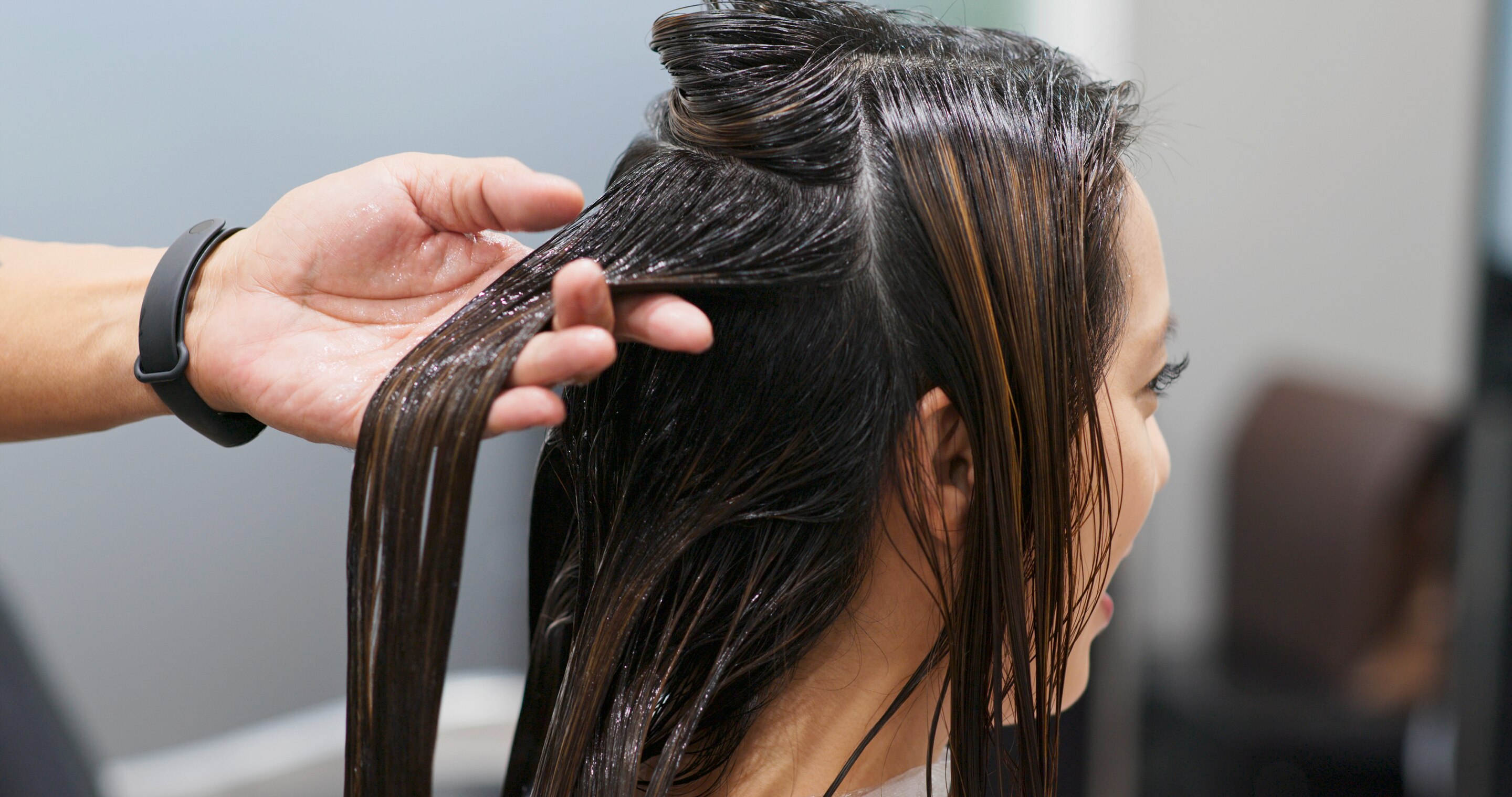 A woman gets her hair treatment at the salon; a man’s hand holding her hair.