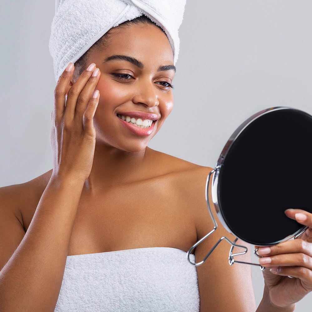 Dark skinned woman in towel touching her face