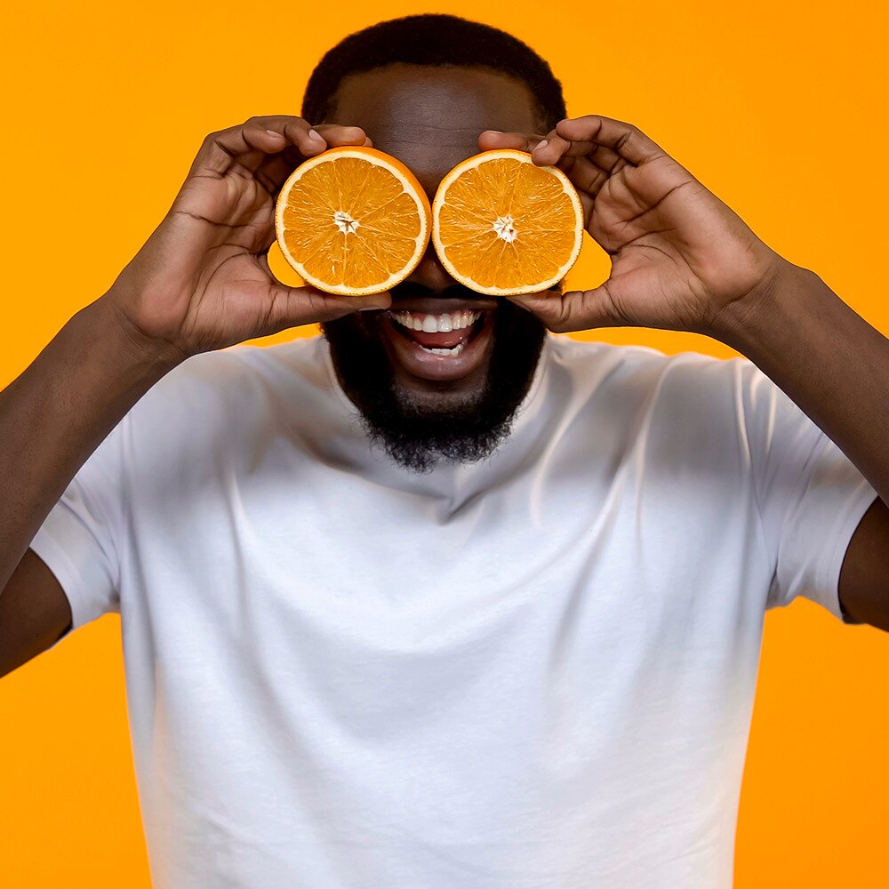 Dark skinned man holding oranges over his eyes