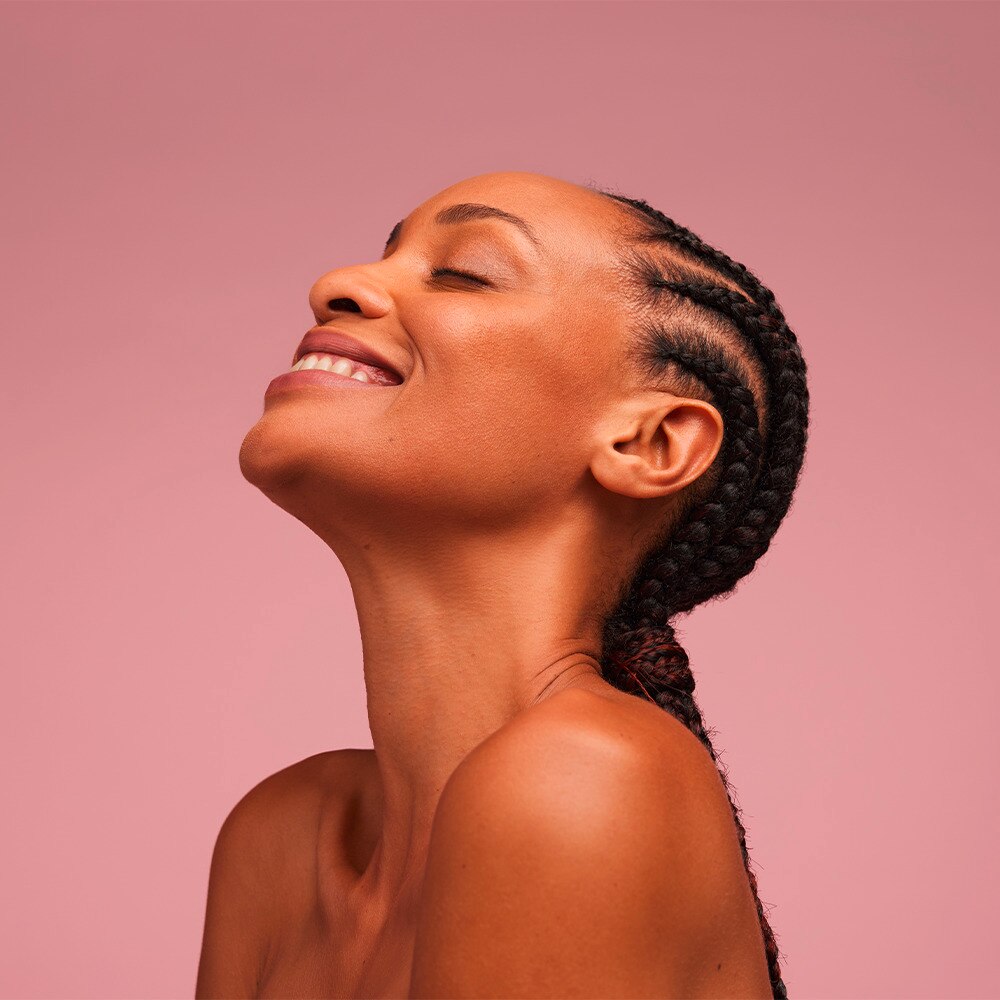 Woman with healthy skin smiling against pink backround
