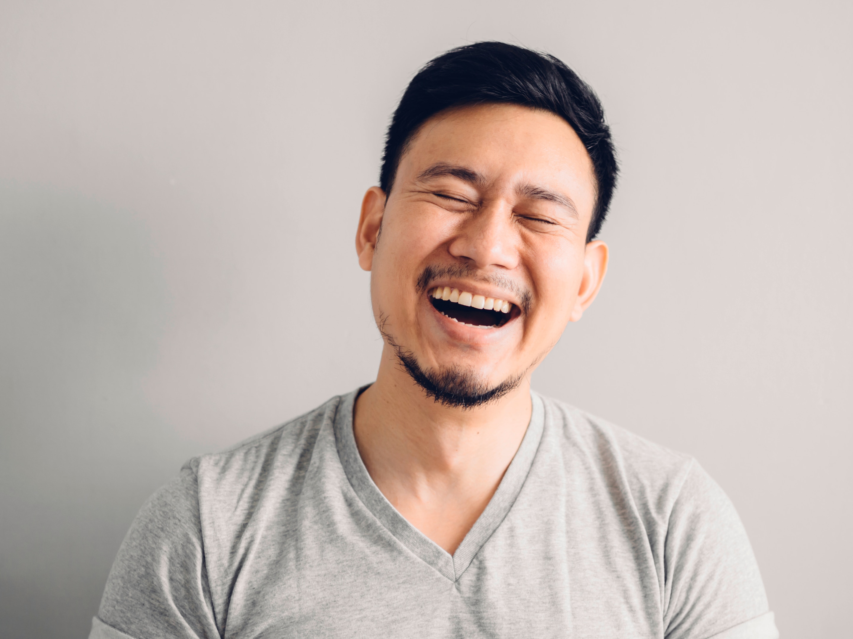  Asian man with facial hair and wearing gray t shirt laughing