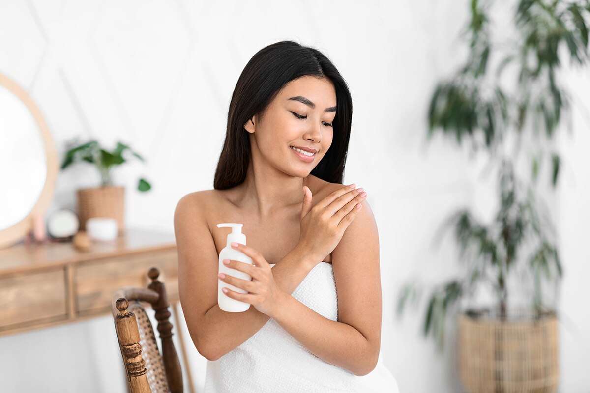 Asian woman smiling and applying body lotion