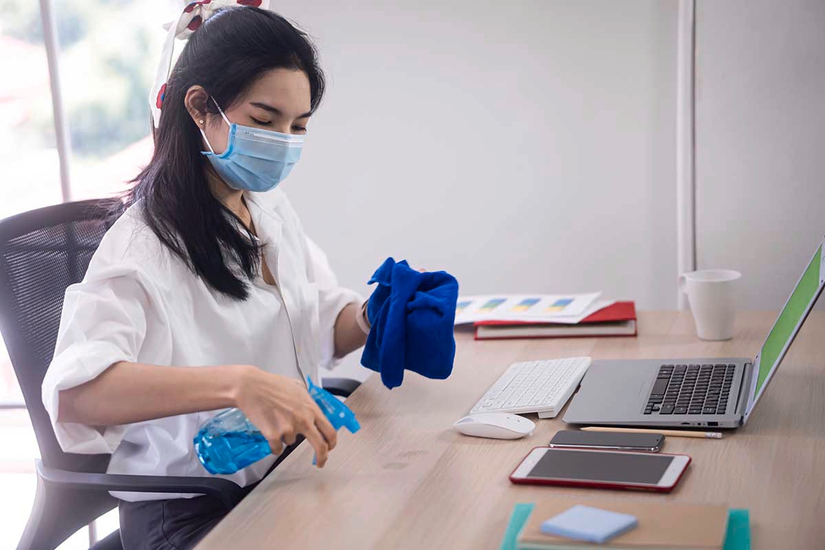 Asian woman wearing mask and spraying alcohol on her desk