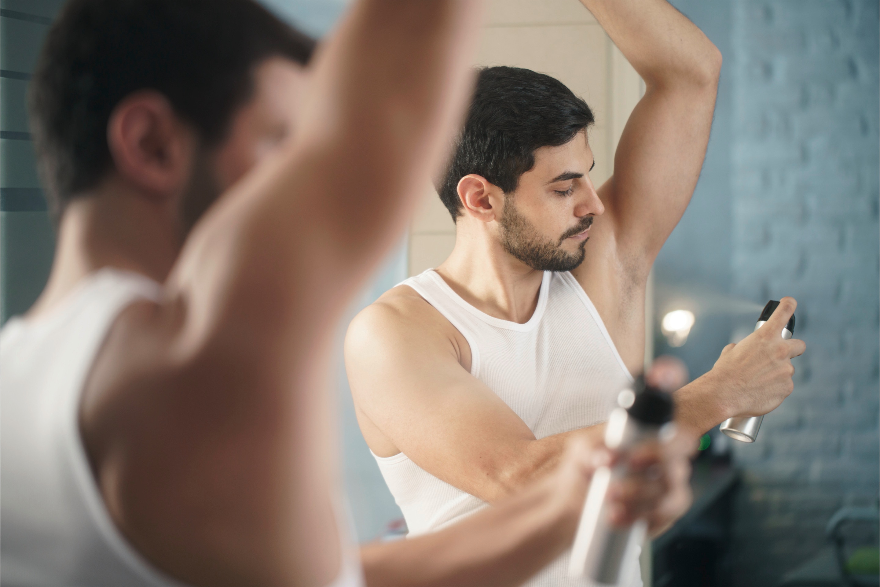 pria sedang menyemprotkan parfum deodorant body spray ke ketiak
