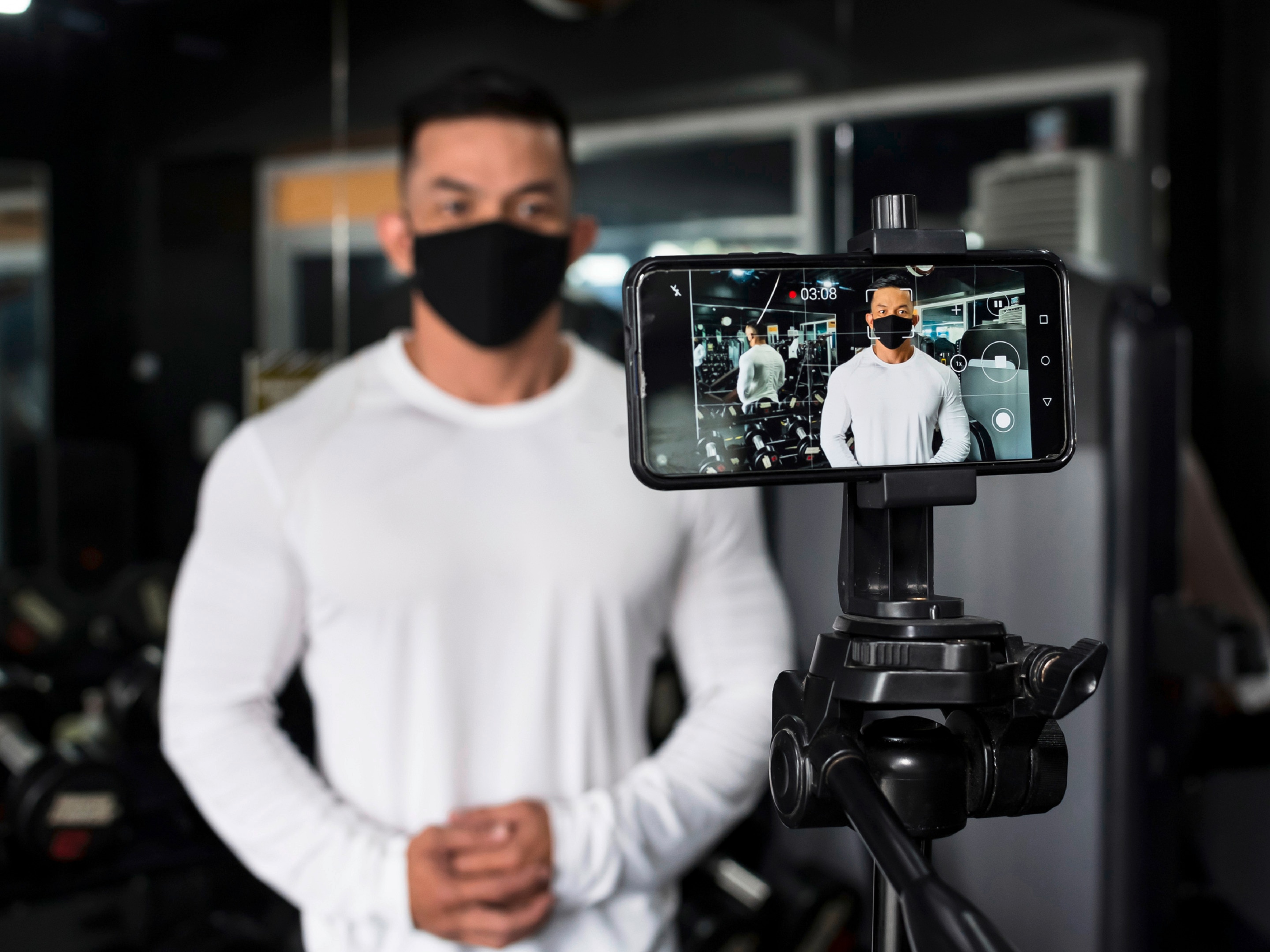 youtuber pria sedang merekam diri sendiri dengan bantuan tripod dan smartphone