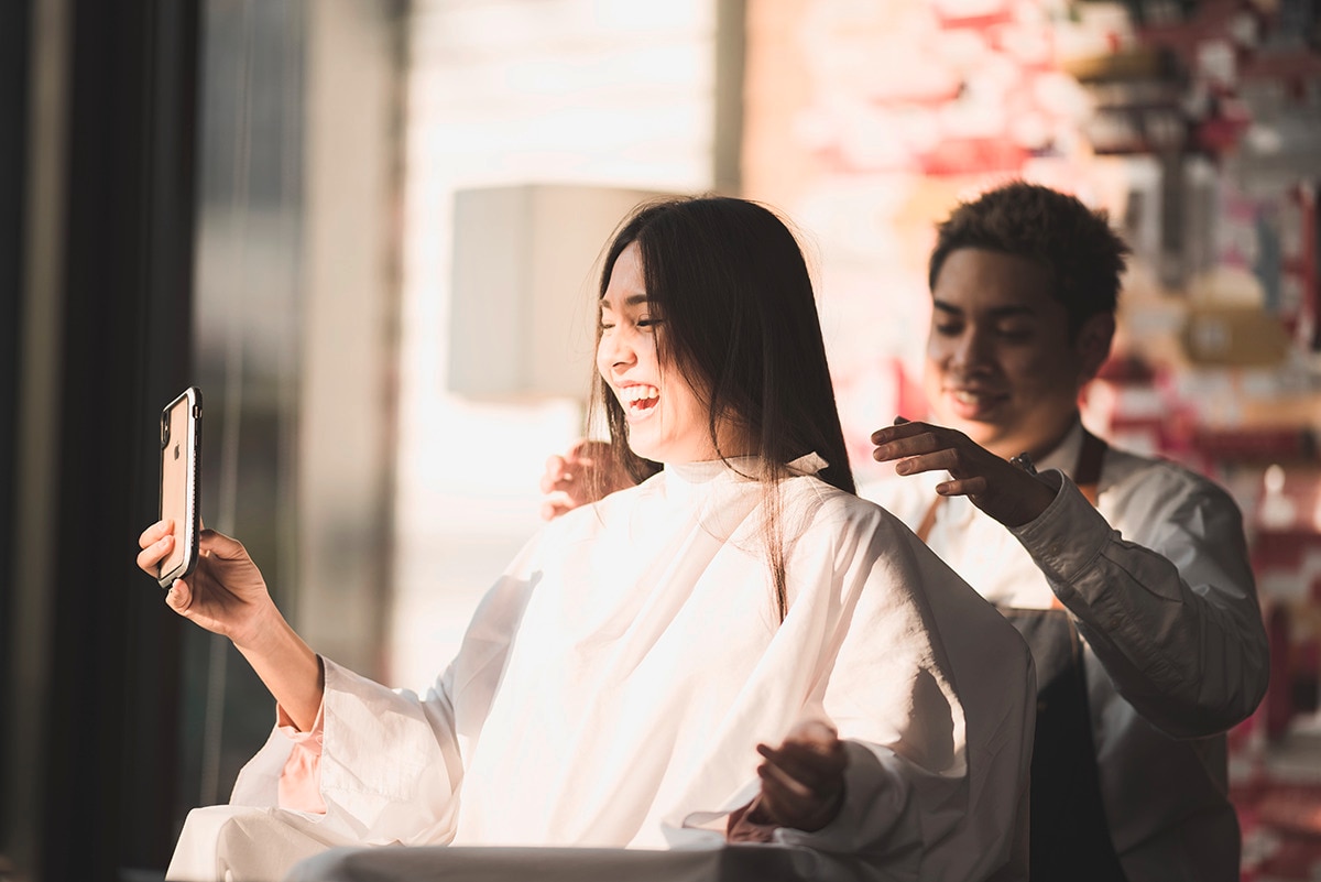 Asian woman talking on her phone while getting hair cut