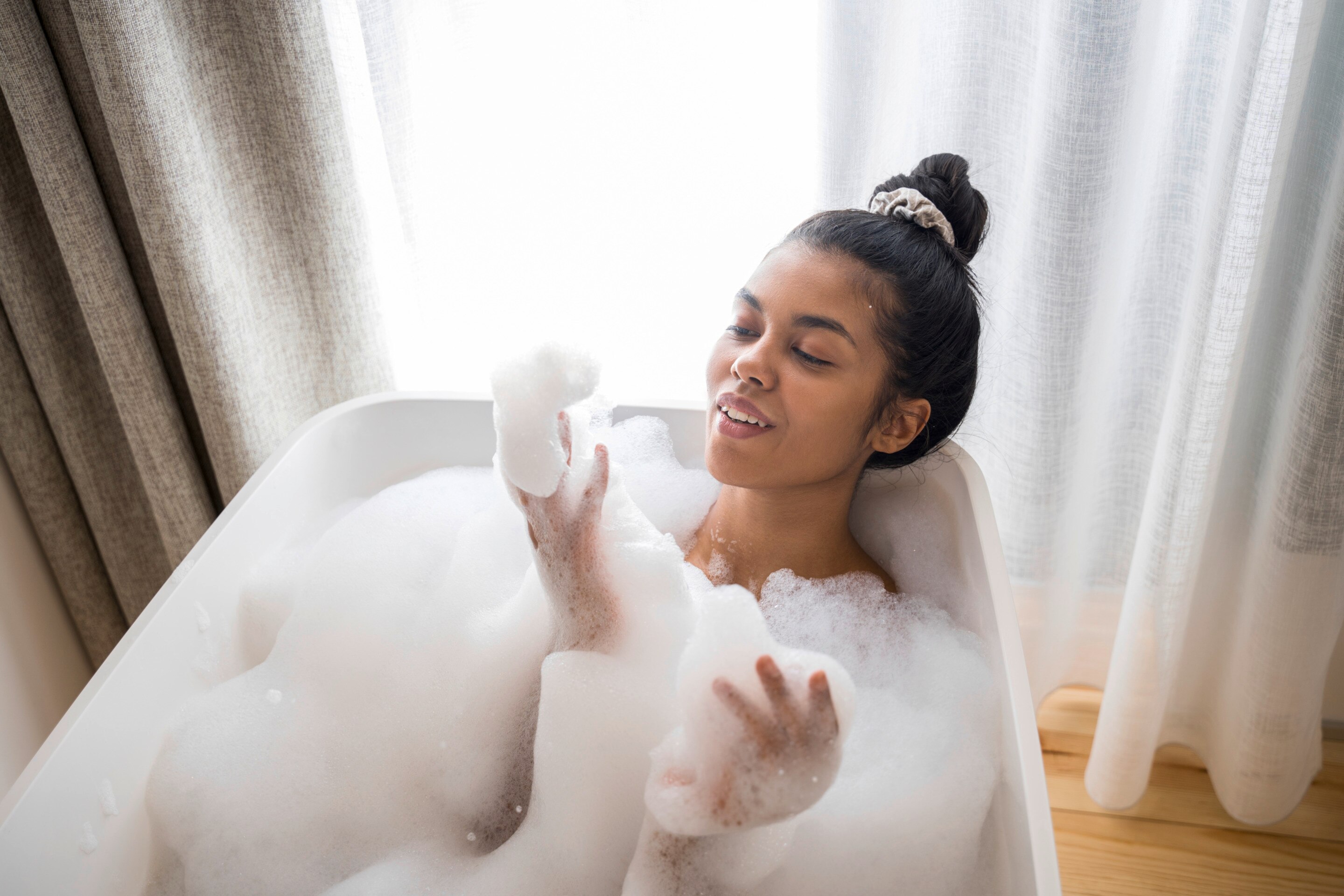 An Asian woman with a top bun in a bubble bath