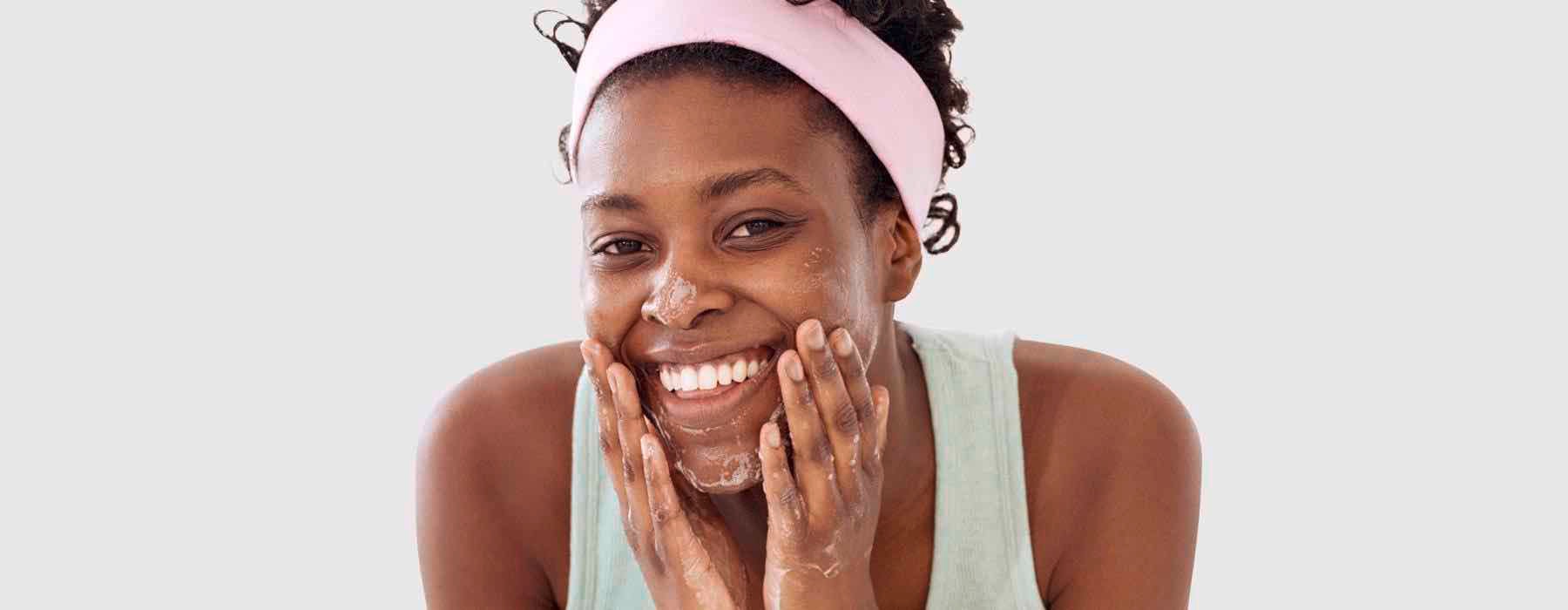 A woman smiling towards the camera and cleansing her face