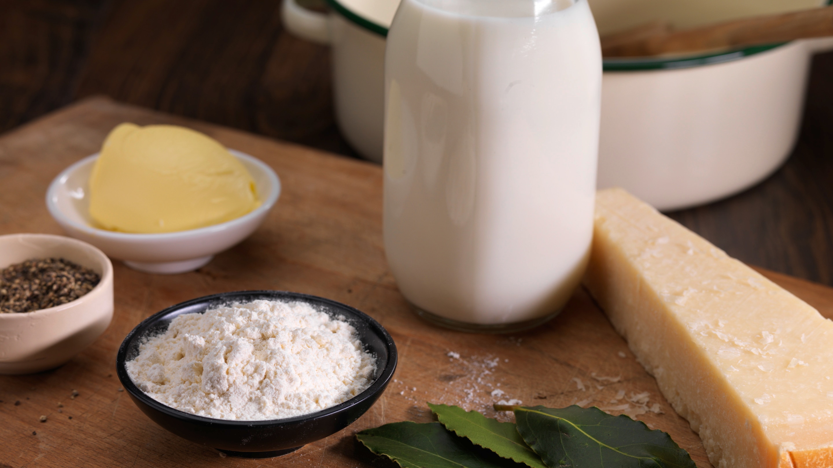 Raw ingredients (cheese, milk, flour, butter) for bechamel sauce on wooden surface.