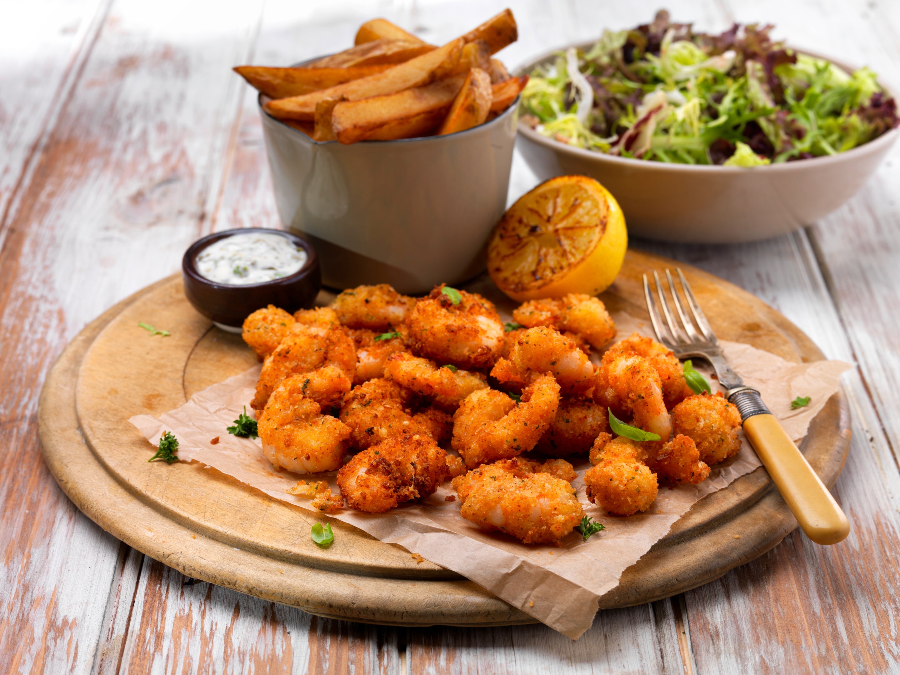 Breaded scampi on a serving board with chips, salad, lemon and dip