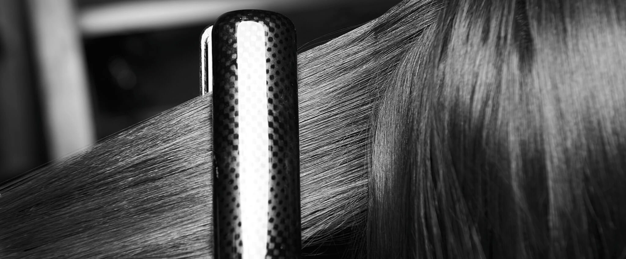 Pramen dlouhých tmavých poškozených vlasů narovnávaný žehličkou.