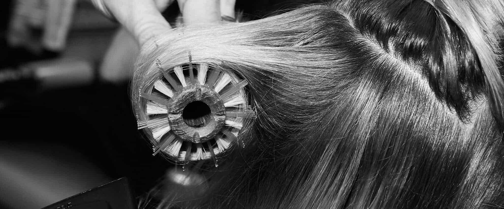 Primer plano del cabello delgado de una modelo al que están peinando con un cepillo y secadora.