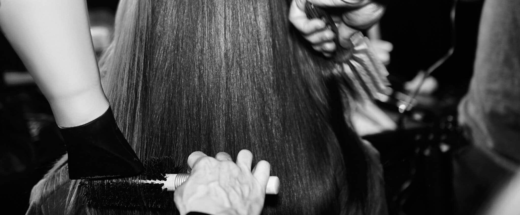 Dos estilistas usan un cepillo y un secador para peinar el cabello de una mujer.