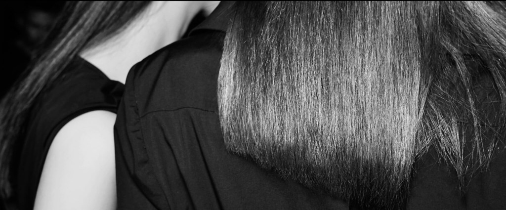 A stylist applies hair spray to a model's long dark, oily hair. 