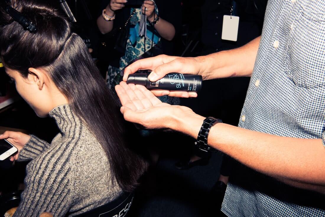 Egy stylist hajformázó terméket visz fel egy ülő modell feltűzött hajára.
