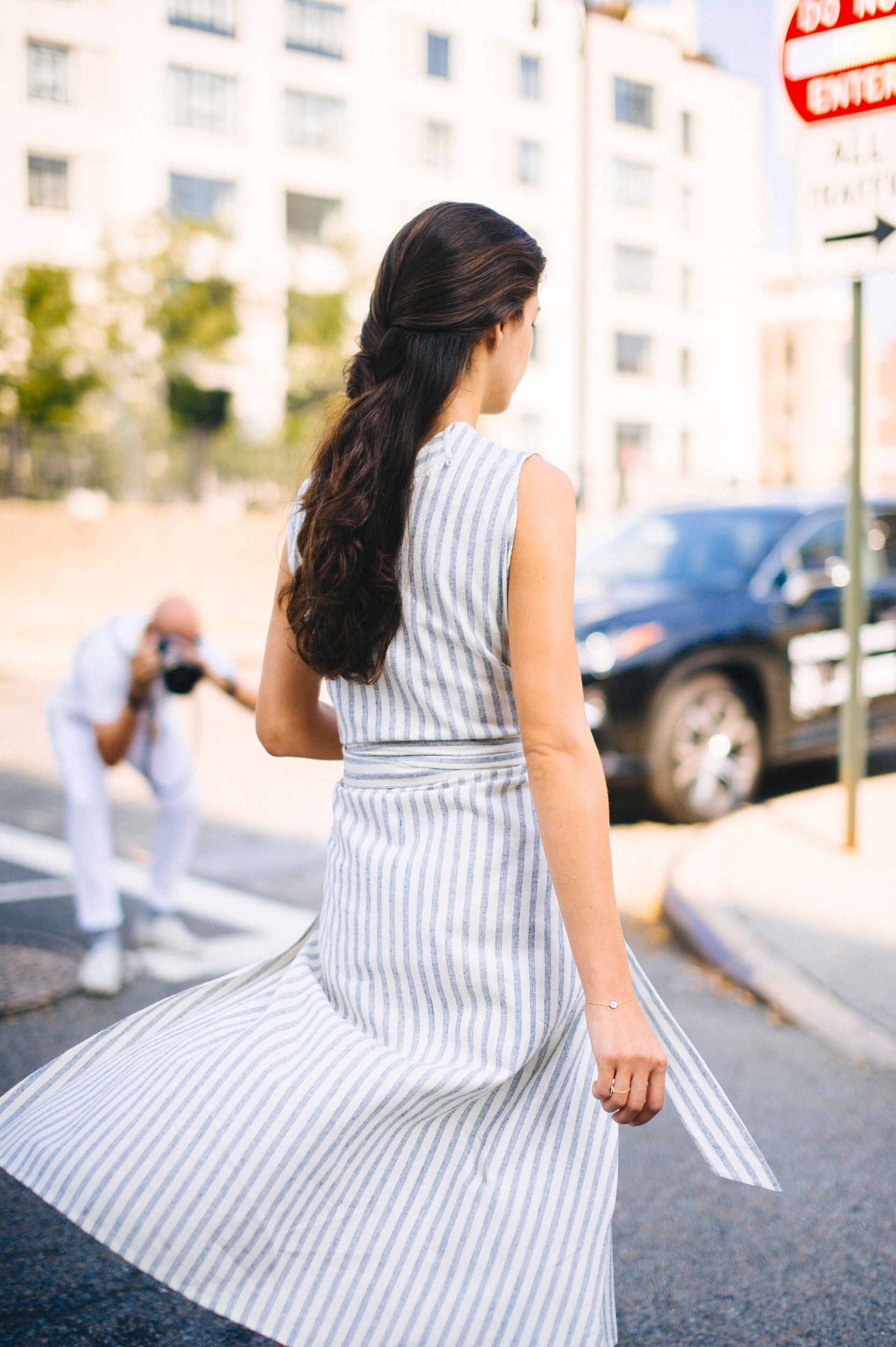 A woman walking down the street with her hair in a thick braid and a photographer taking her picture
