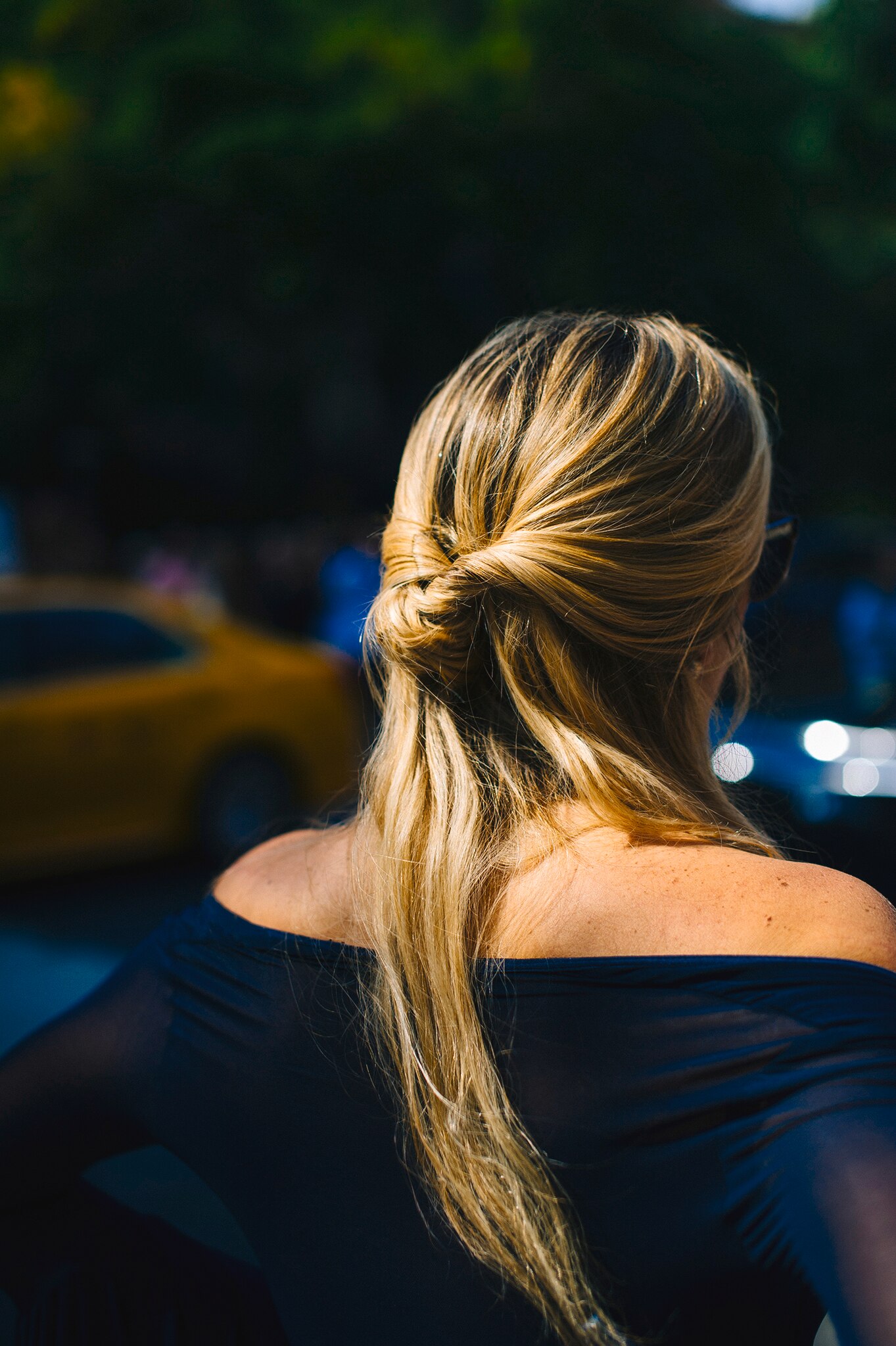 A blonde woman walking through the city, wearing a blue blouse with her hair in a messy bun