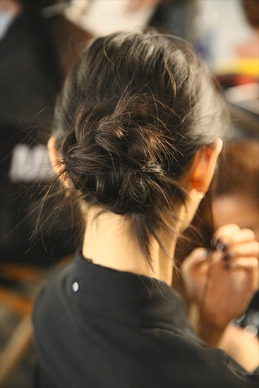 A model with her damp, long brown hair being sprayed with product by a stylist just out of shot