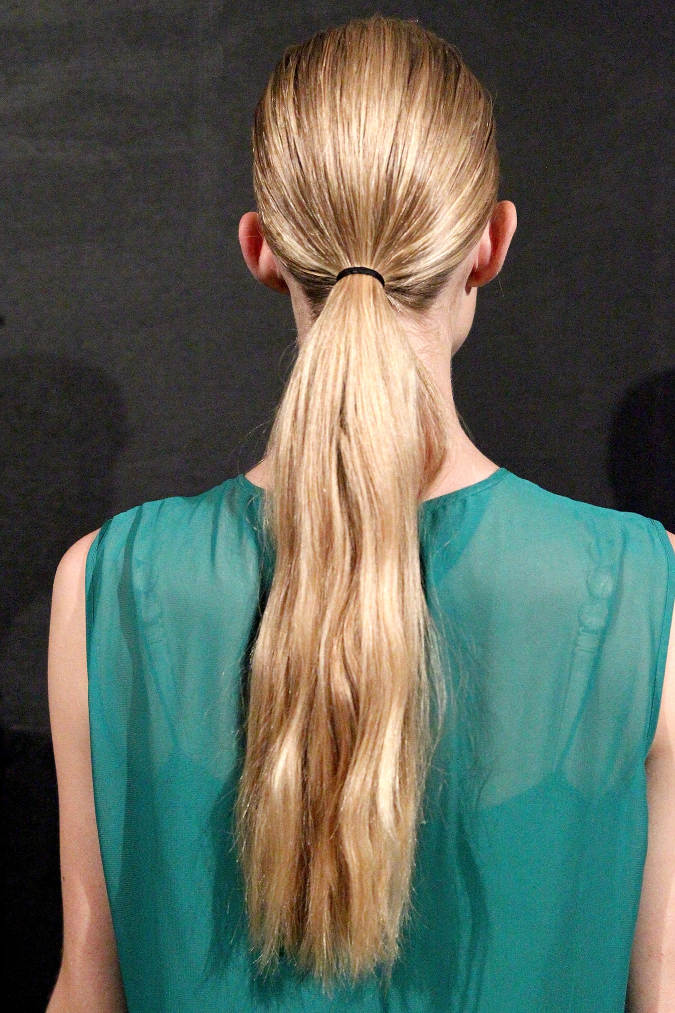 A blonde model wearing a green blouse with her hair in a low ponytail 