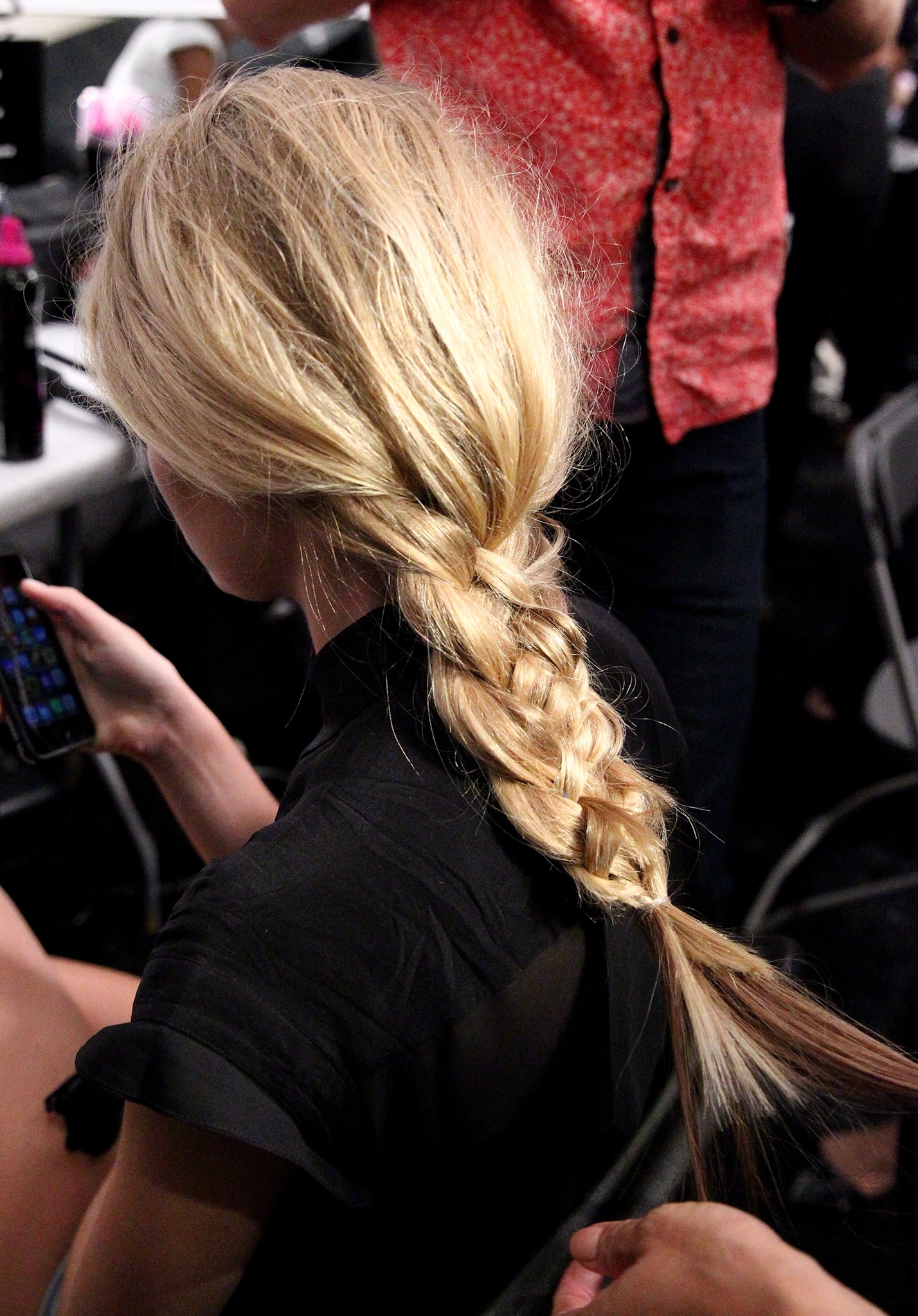 A blonde model sitting down backstage with her hair in a long, thick braid